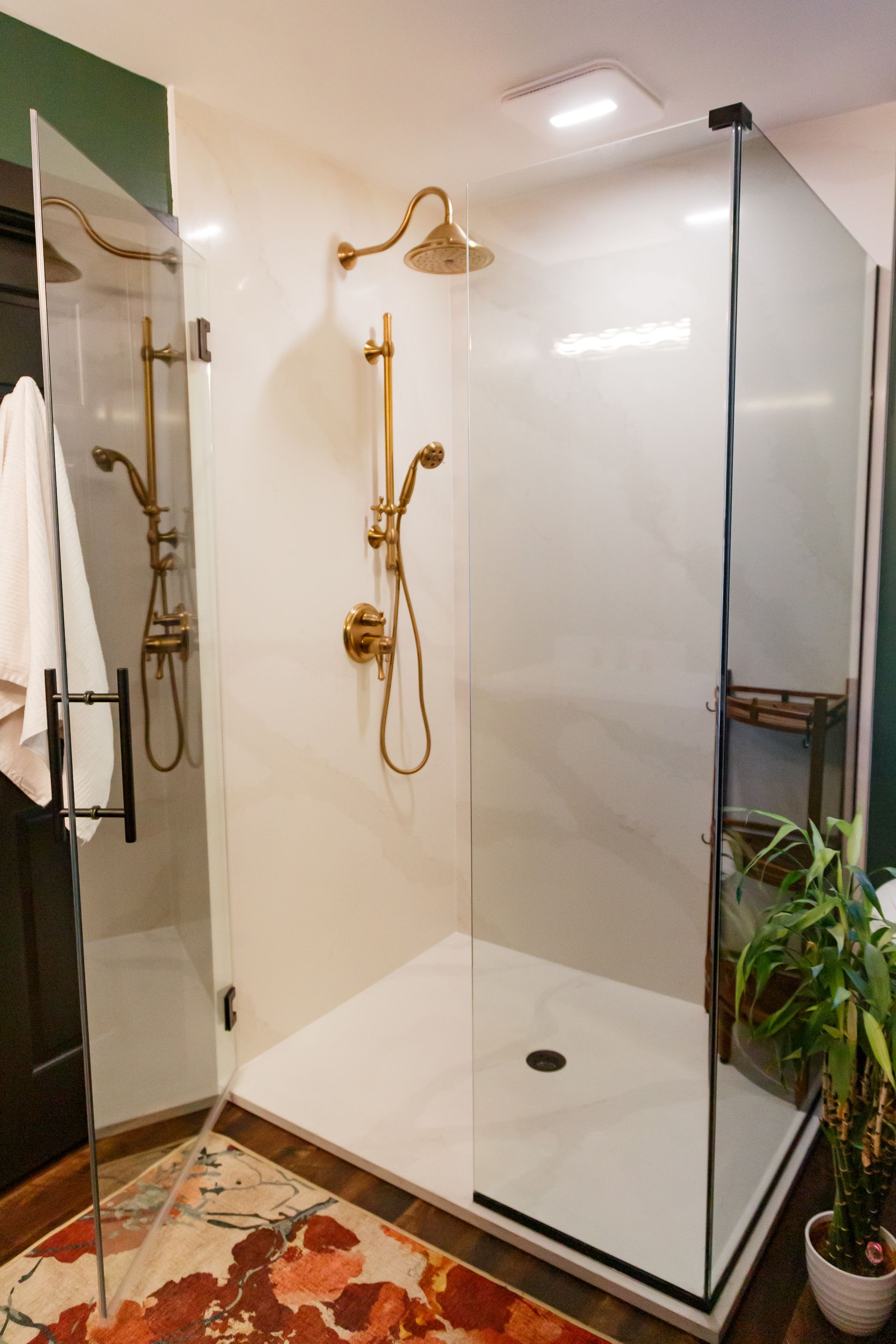A bright, modern shower with gold fixtures and clear glass doors. The white interior contrasts with a colorful rug.