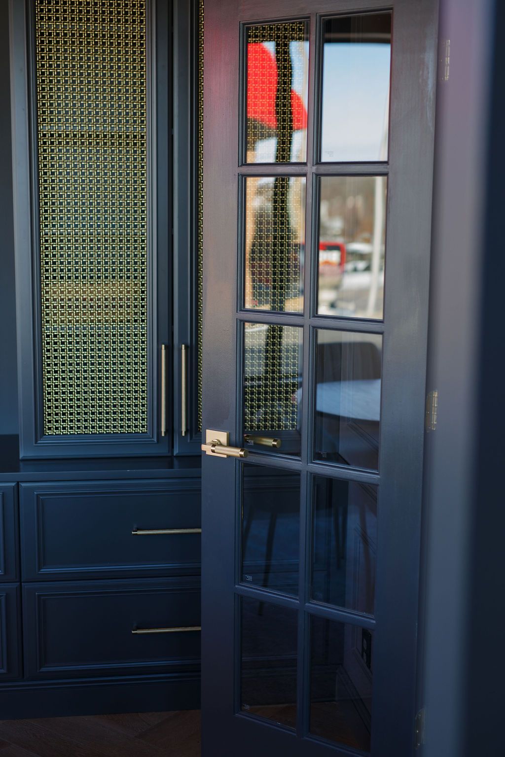 Dark blue cabinets with brass hardware. French door with glass panes. Gold mesh backing.