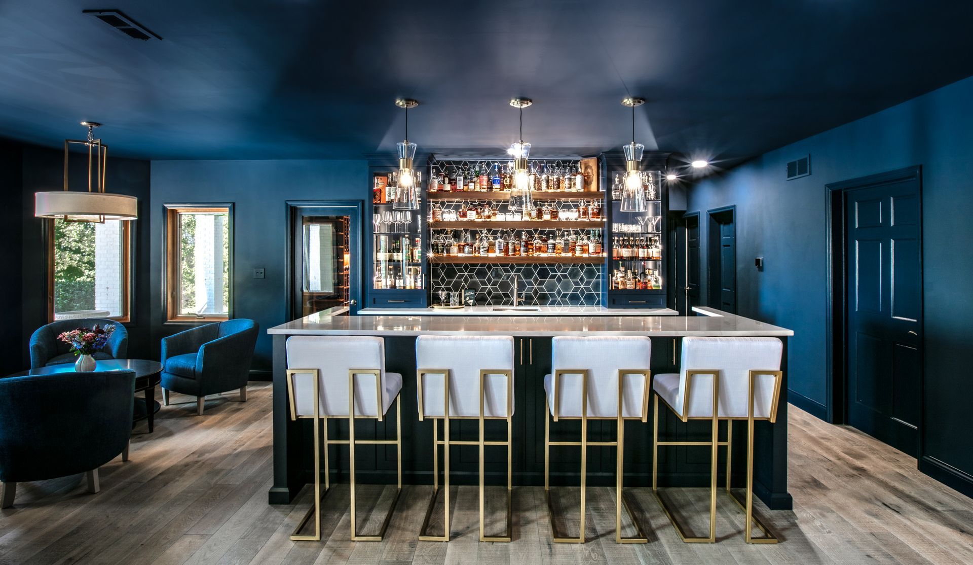 Bar area with dark blue walls, a bar with stools, and bottles on shelves.