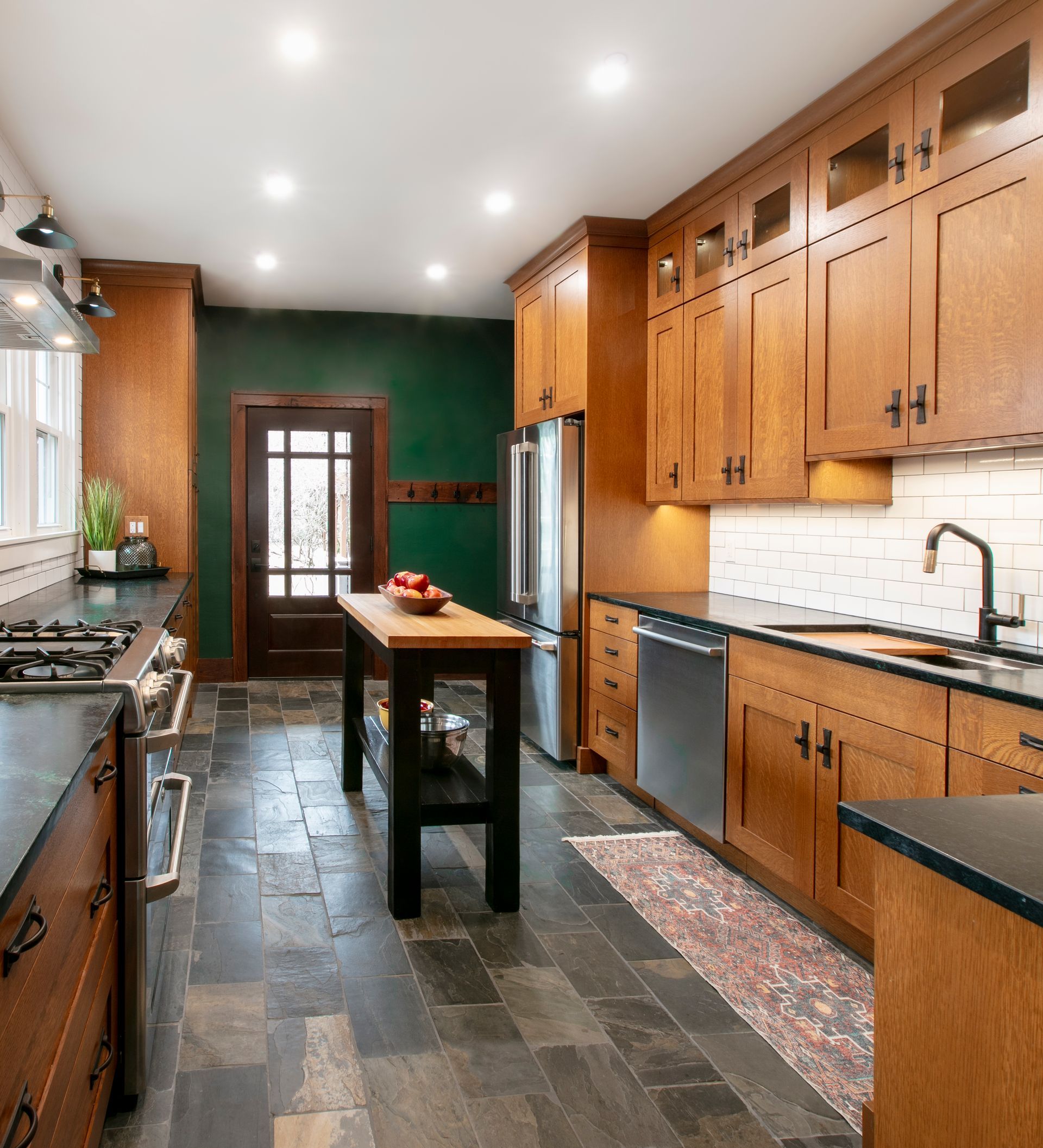 Kitchen with wood cabinets, dark countertops, slate tile floor, and a dark green wall.