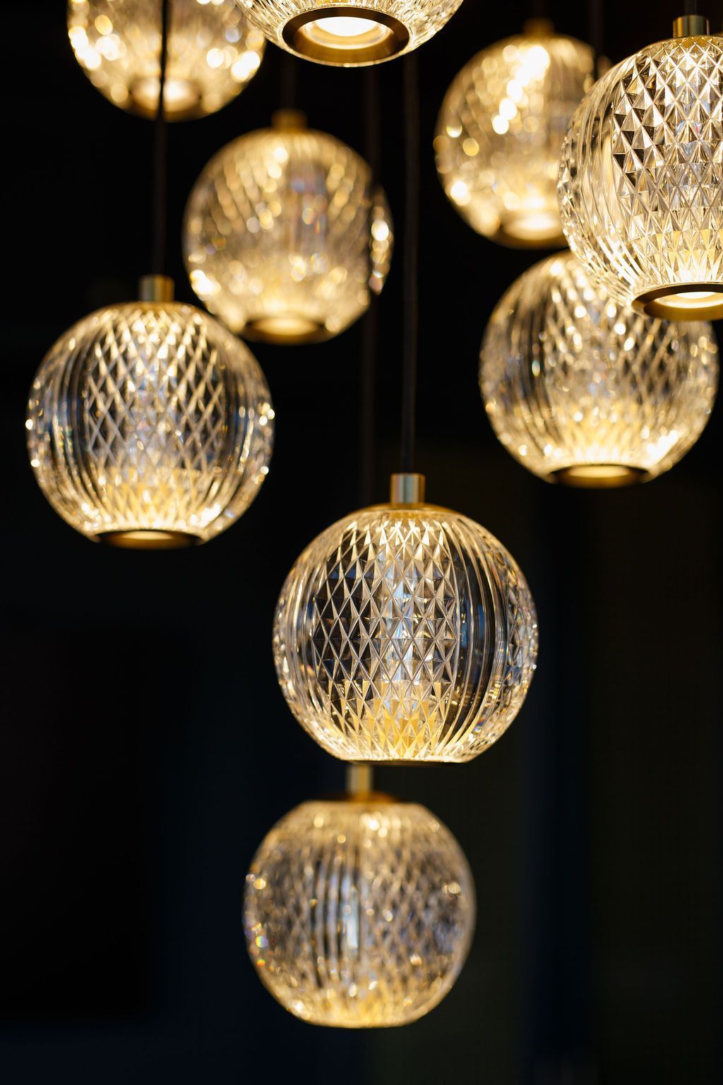 Close-up of a cluster of clear, patterned glass globe pendant lights with golden accents, against a dark background.