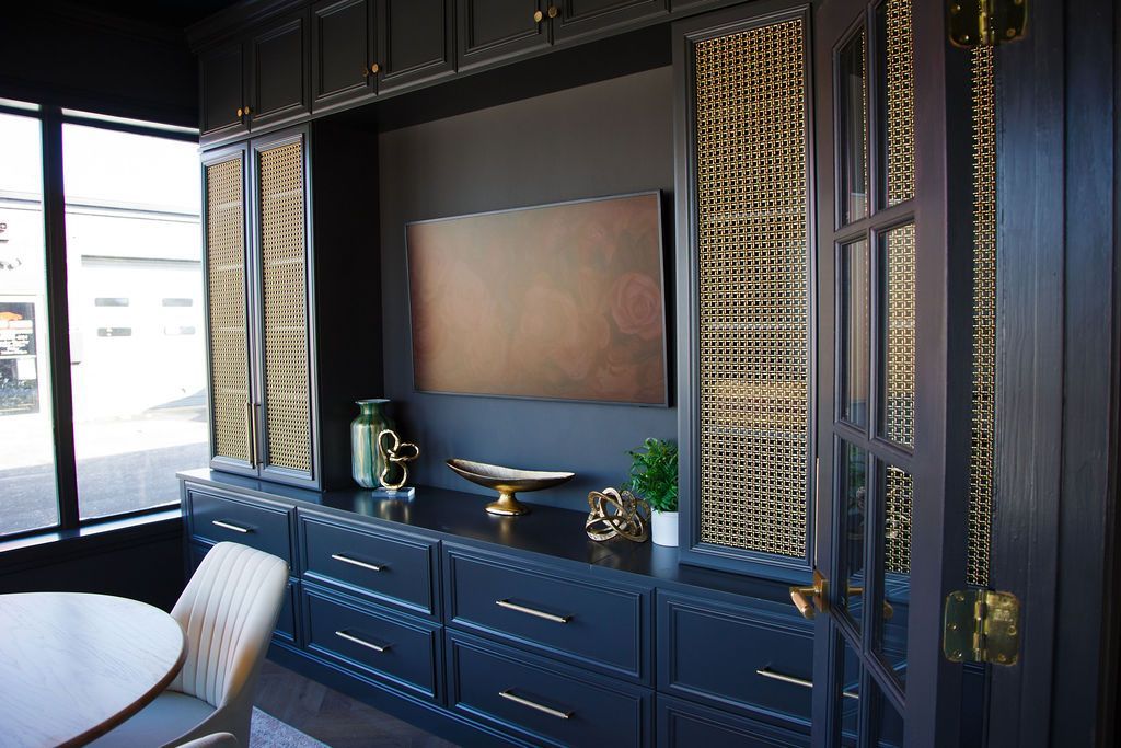 Dark gray entertainment center with gold accents, built-ins, and a television. A window and table are in view.