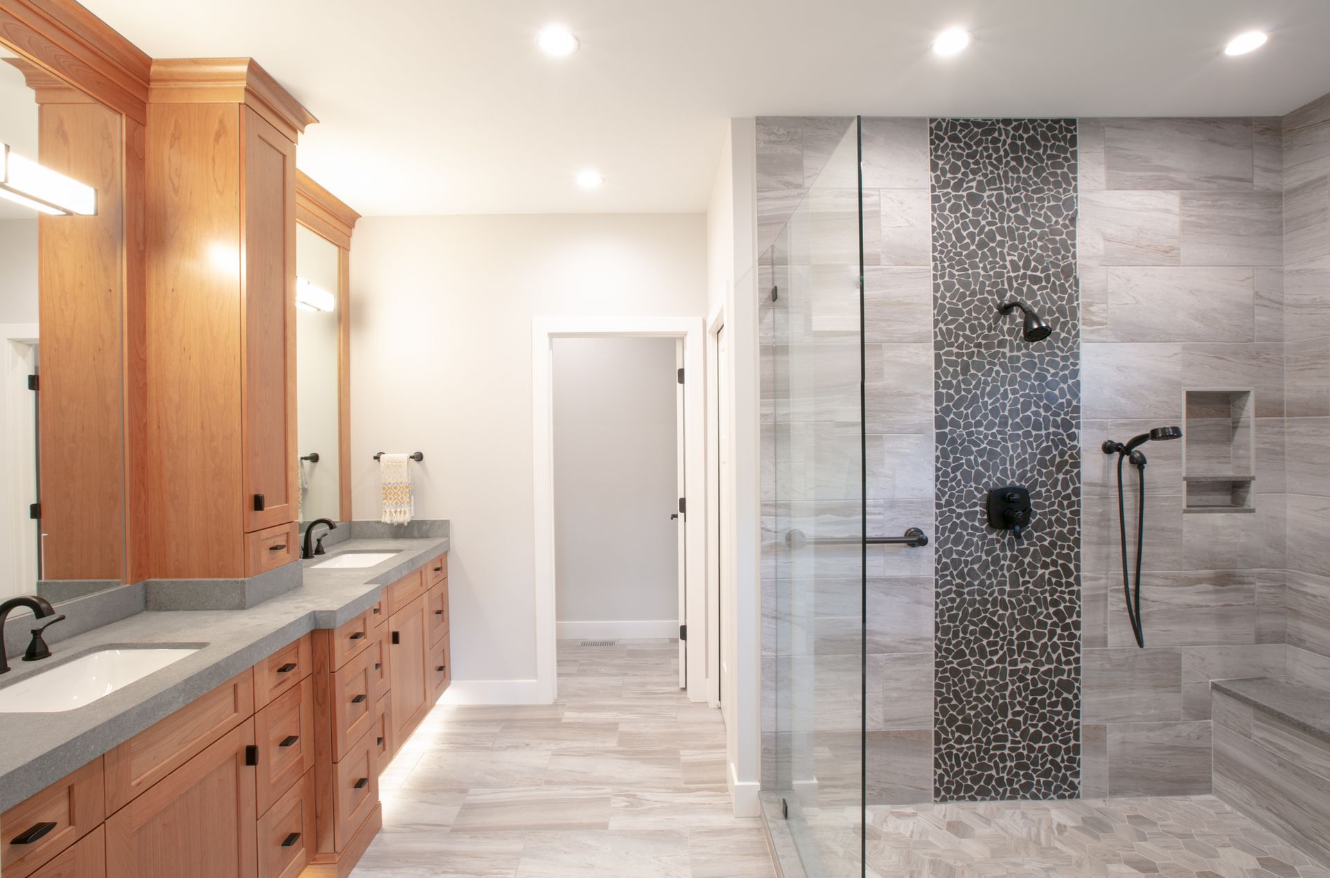 Bathroom with double vanity, large shower with gray tile and pebble accent, and neutral-colored walls.