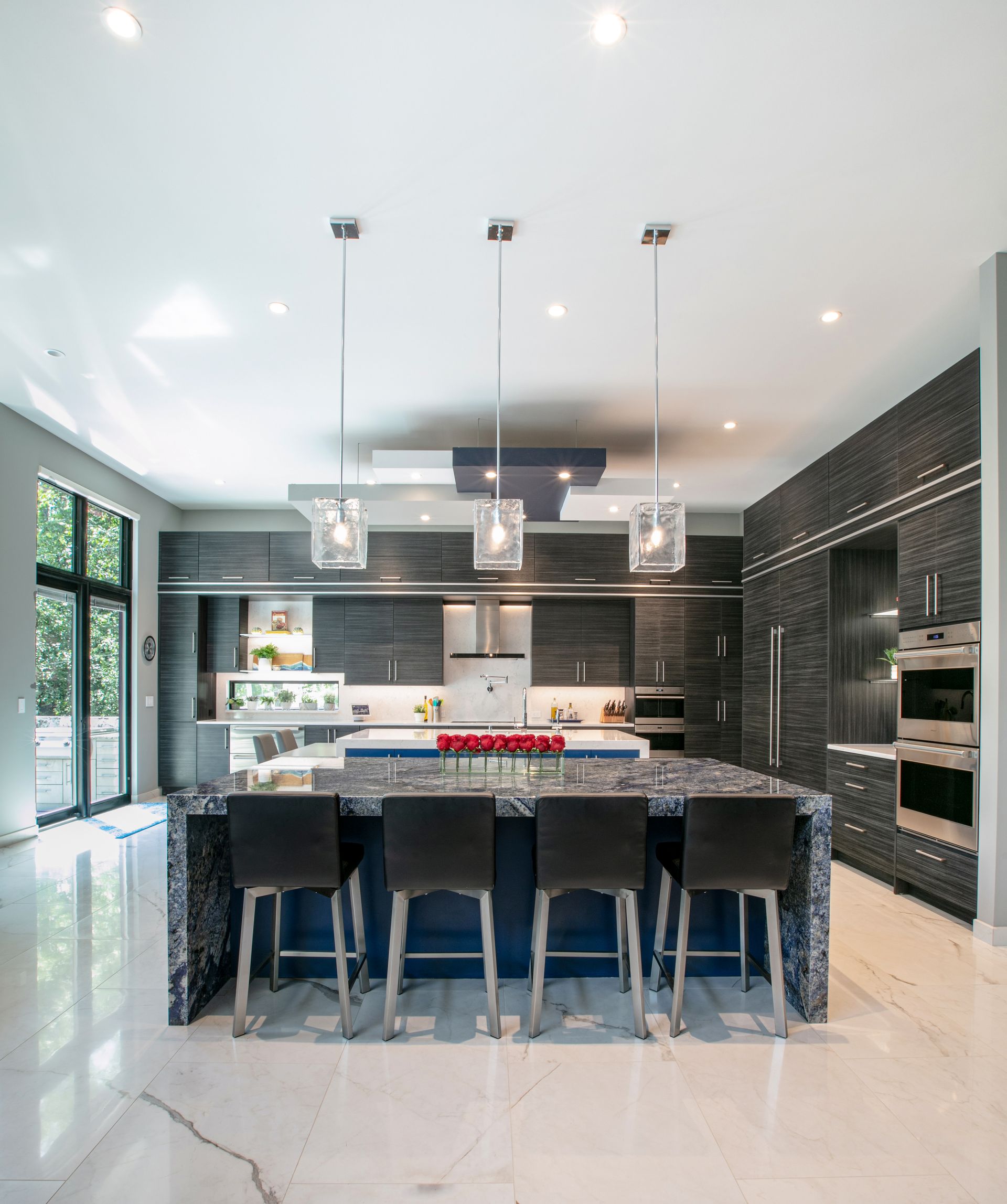 Modern kitchen with blue island, black cabinets, four barstools, pendant lights, and marble floors.