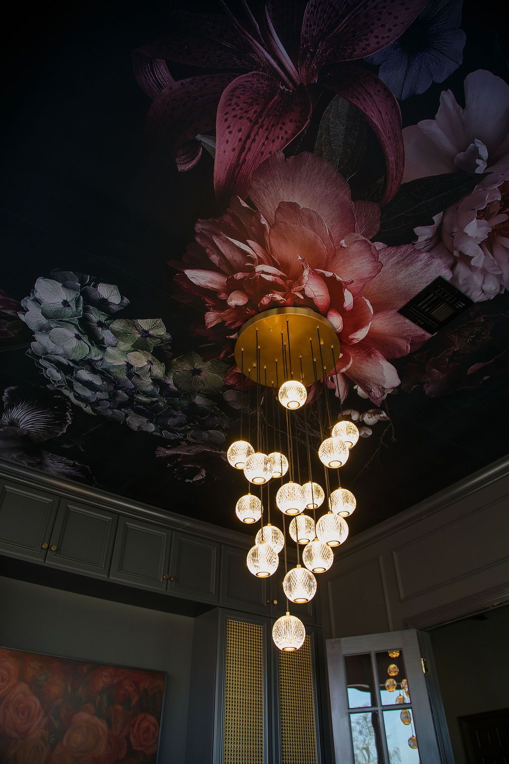 Chandelier with multiple glowing orbs hanging from a floral ceiling mural.