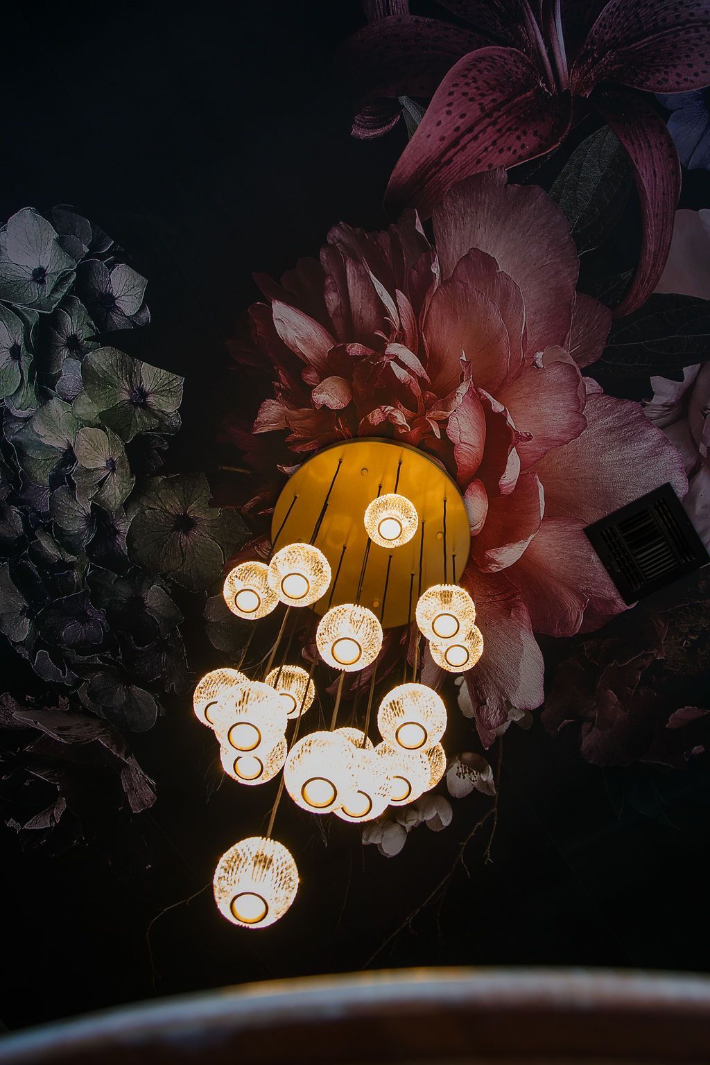 Cluster of orb lights against a floral wallpaper backdrop in shades of pink, burgundy, and dark tones.