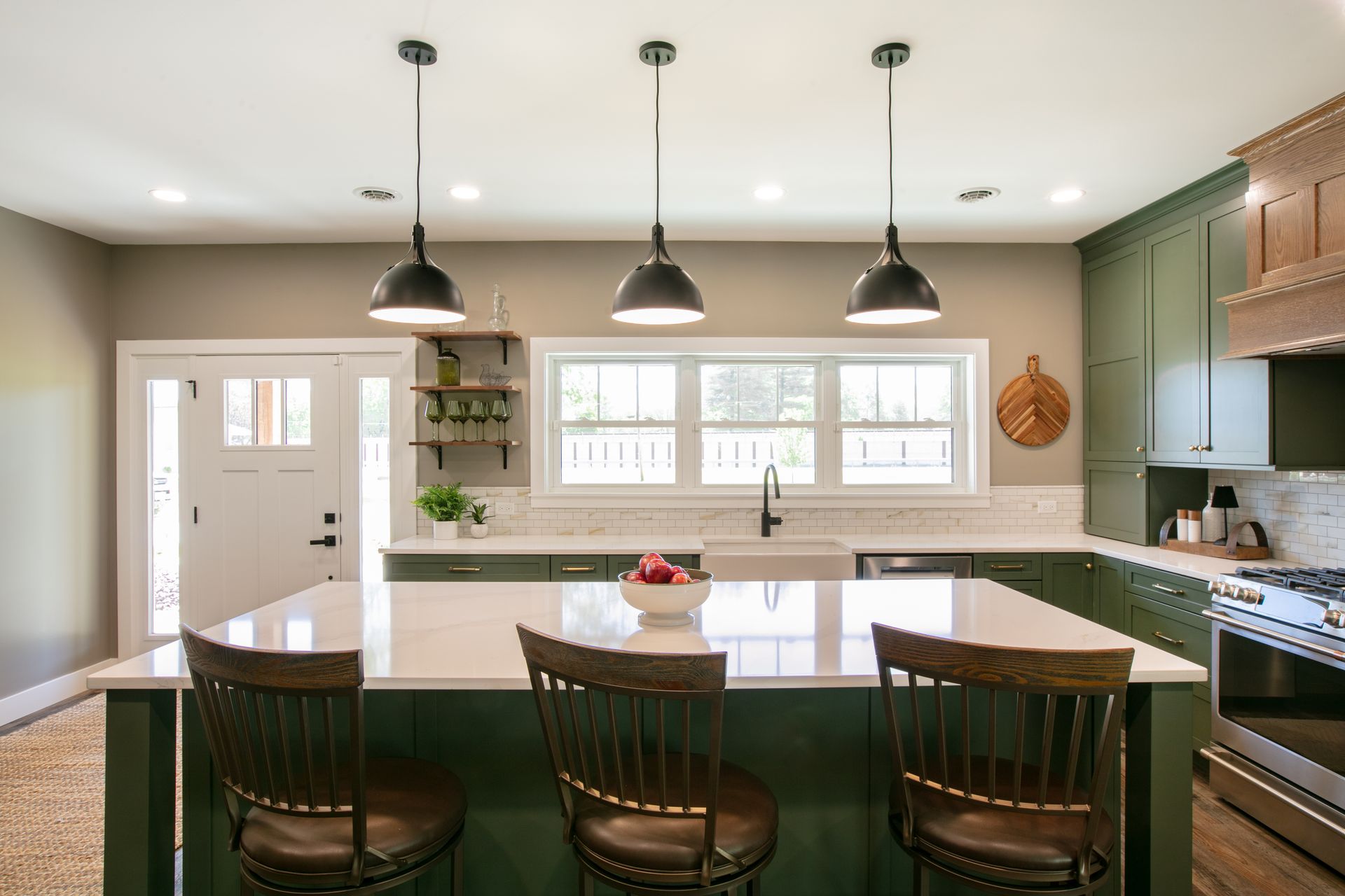 Modern kitchen with green cabinets, white countertops, and three pendant lights over a dark-green island with stools.