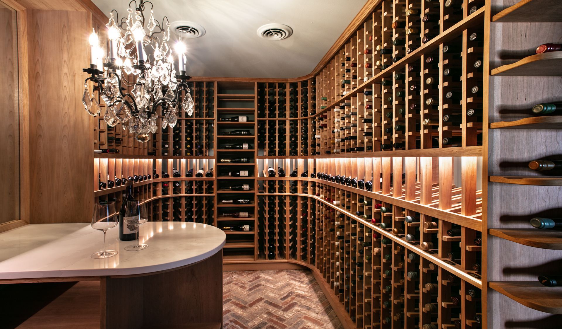 Wine cellar with wooden racks filled with bottles, marble table, chandelier.