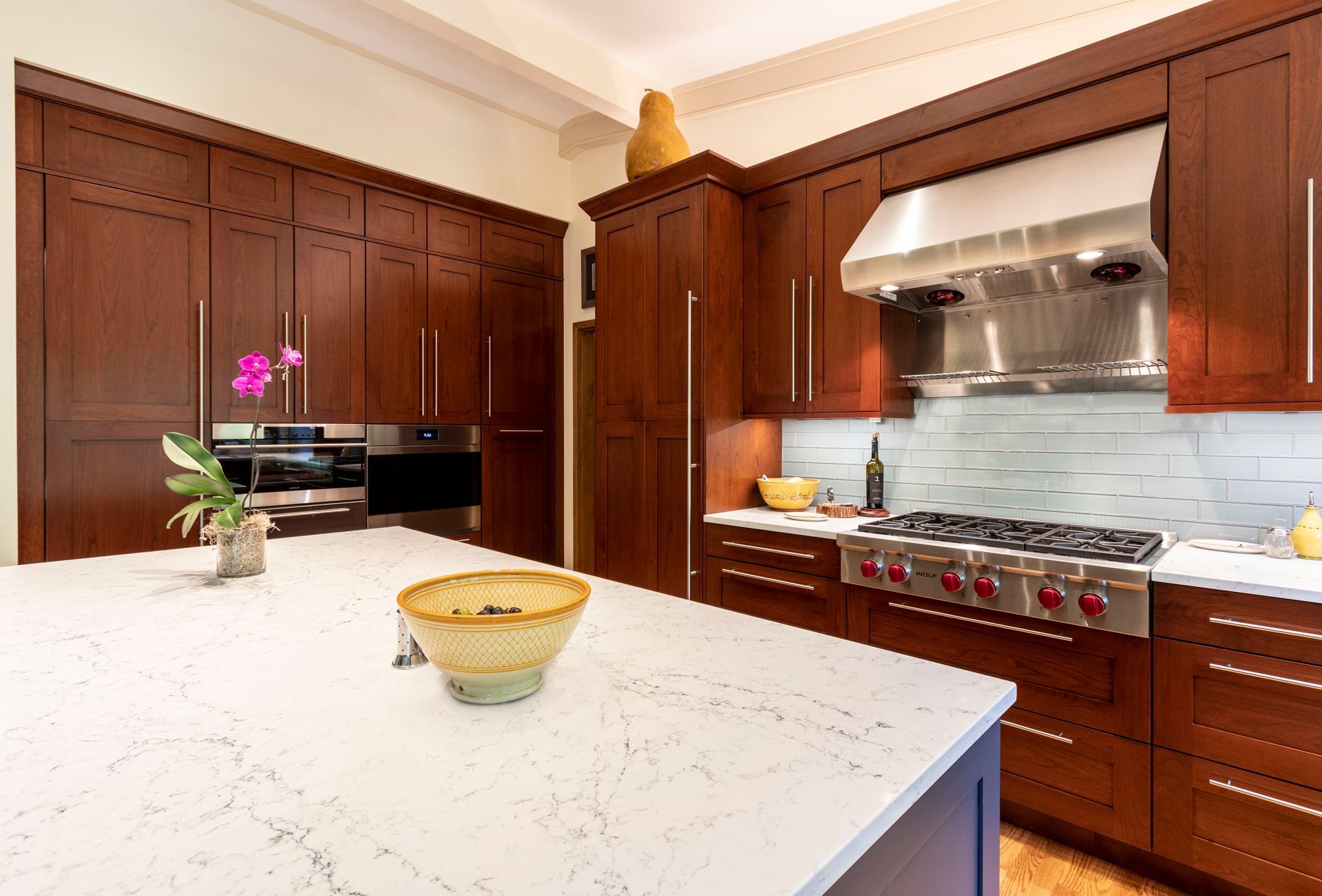 A modern kitchen with dark wood cabinets, white countertops, and stainless steel appliances.