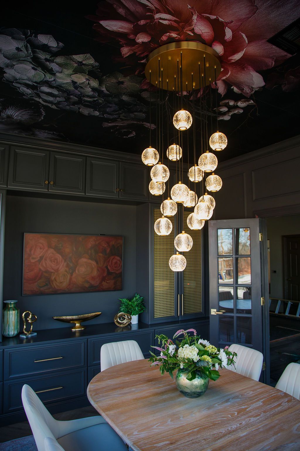 Elegant dining room with floral ceiling, dark walls, a chandelier, and a wooden table.