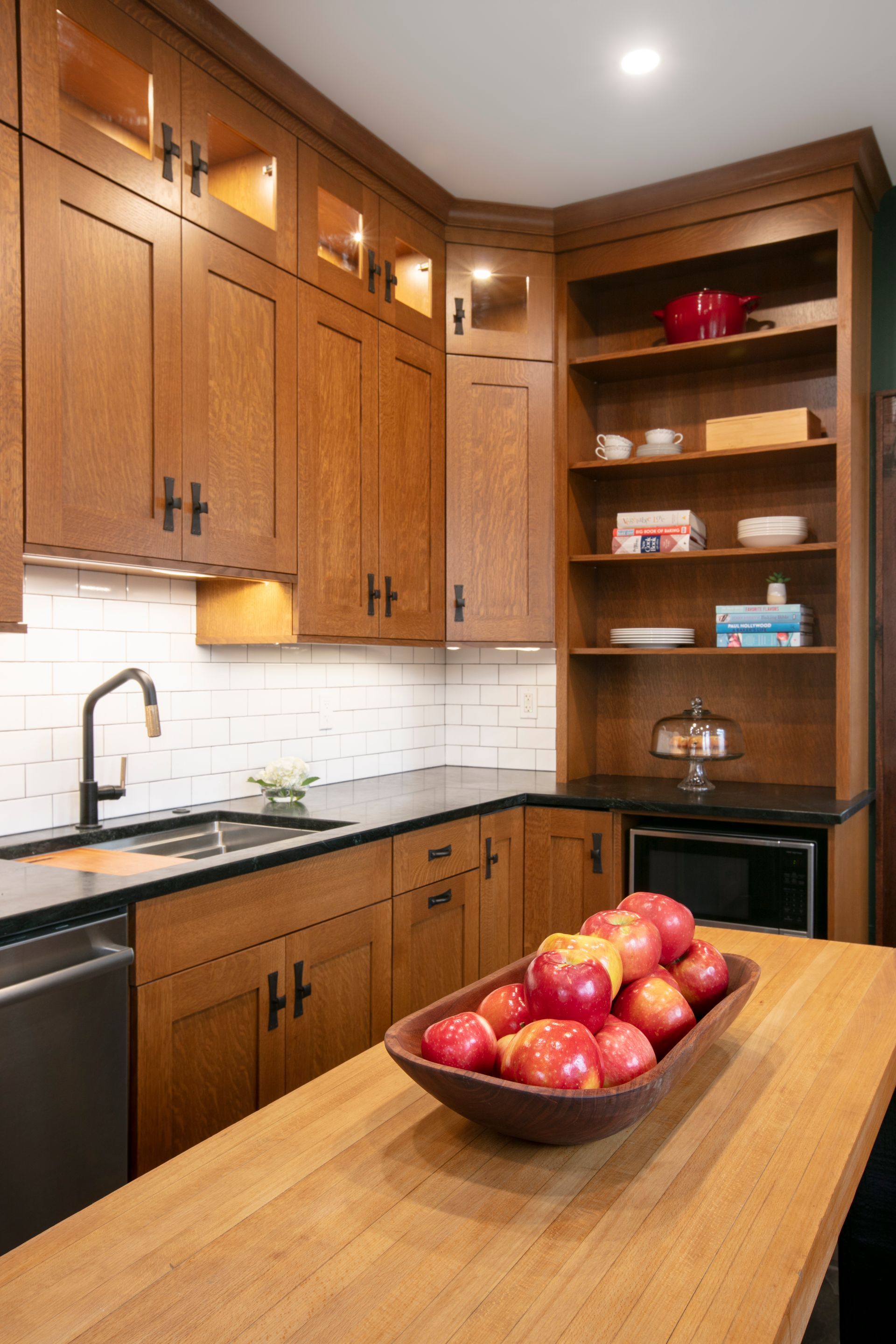Kitchen with brown cabinets, white backsplash, black countertops, wooden bowl of apples on island.