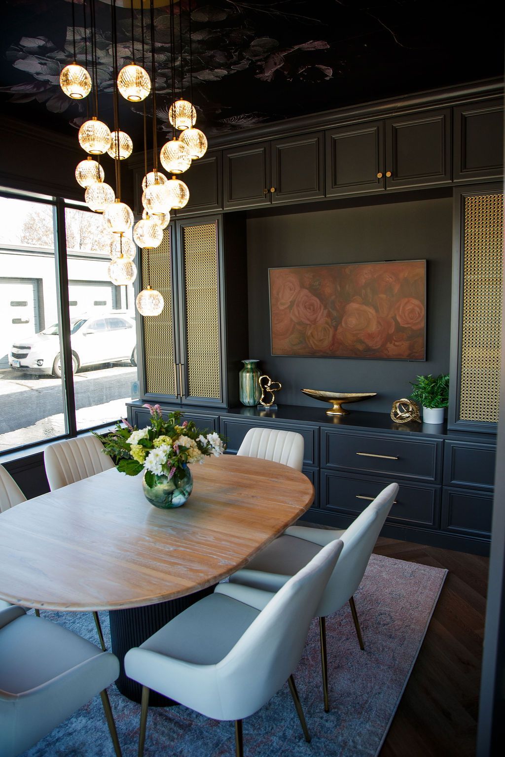 Elegant dining room with oval table, pendant lights, dark cabinets, and large window.