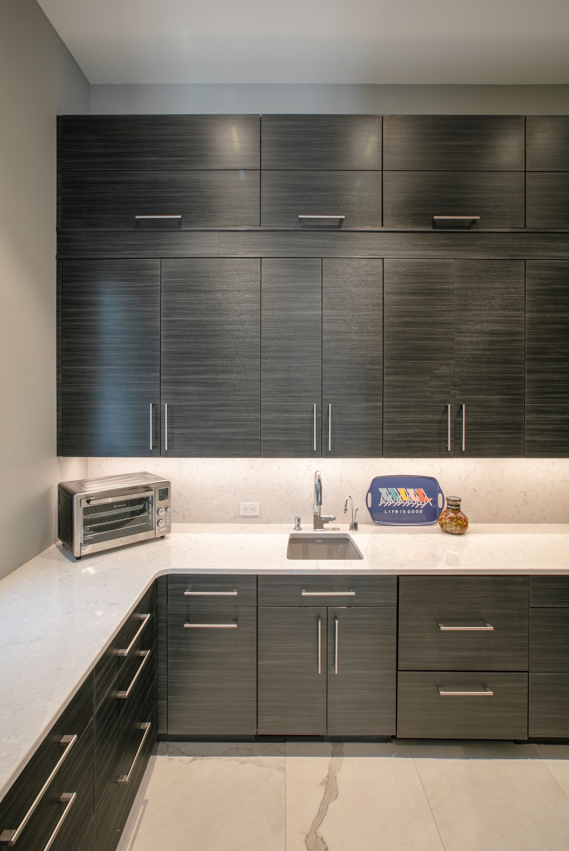 Modern laundry room with dark wood cabinets, a white countertop, and a stainless steel sink.