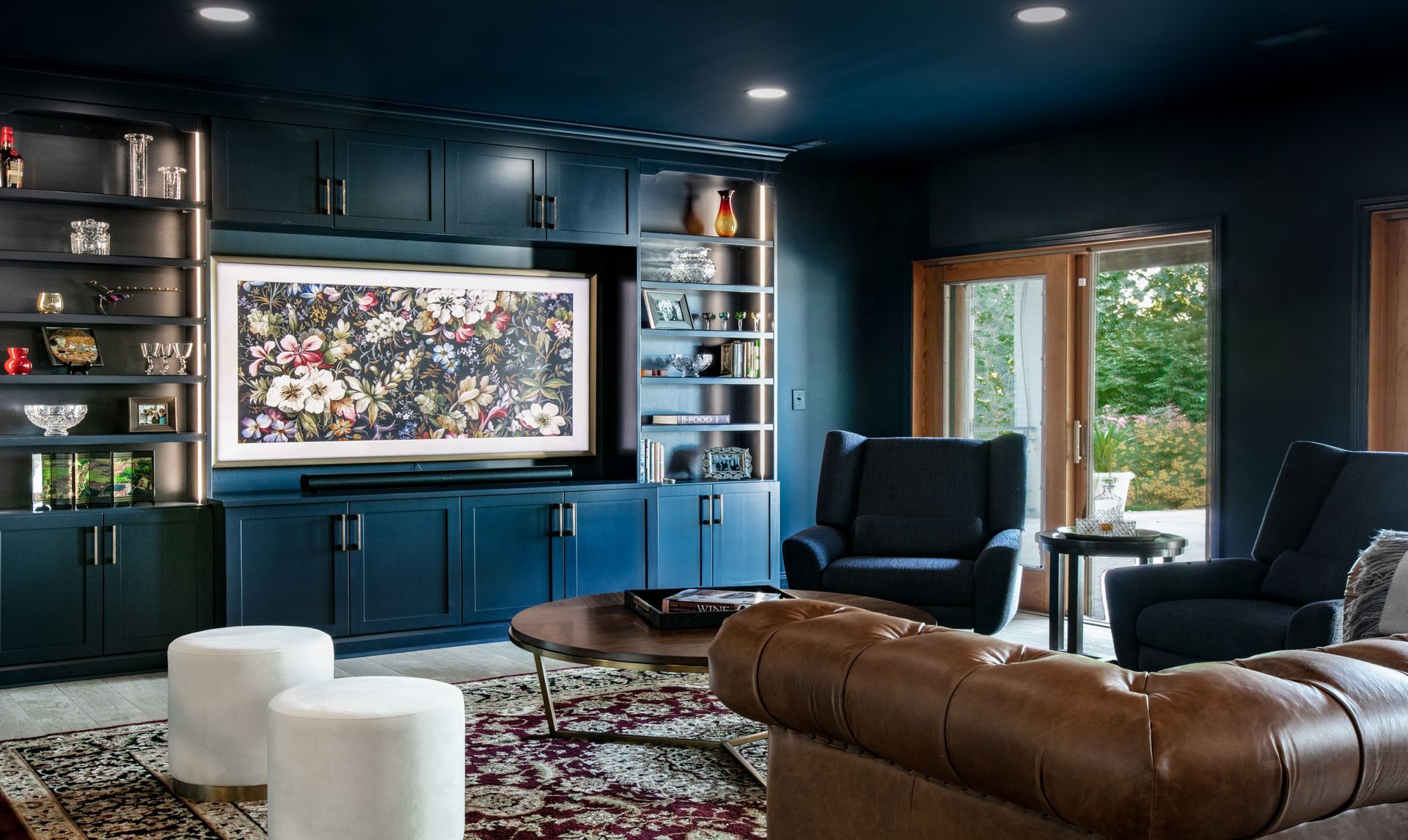 Dark blue media room with built-in storage, large TV, leather sofa, armchairs, and round coffee table.