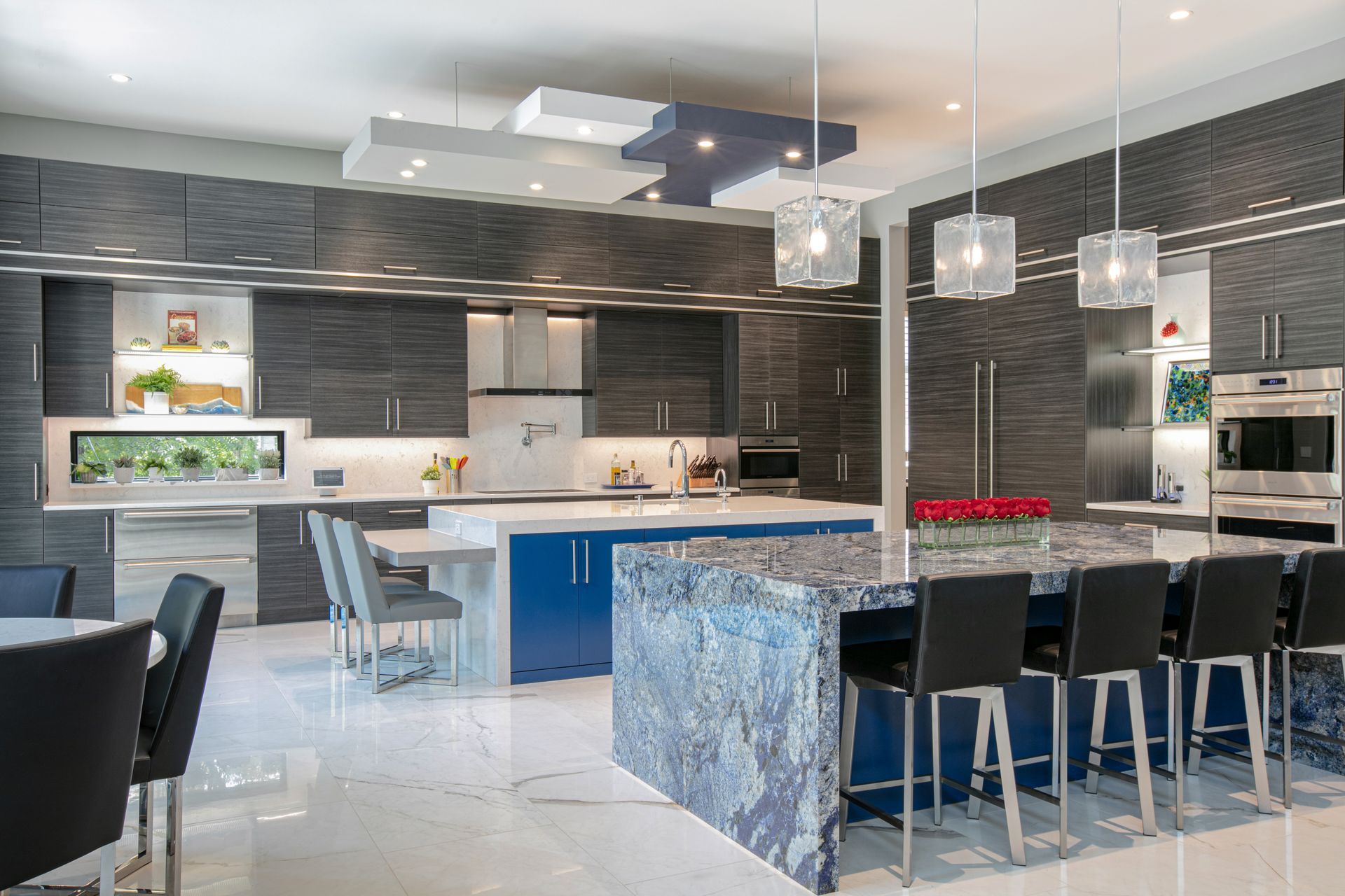 Modern kitchen with blue and gray cabinetry, marble countertops, and a large island with bar seating.
