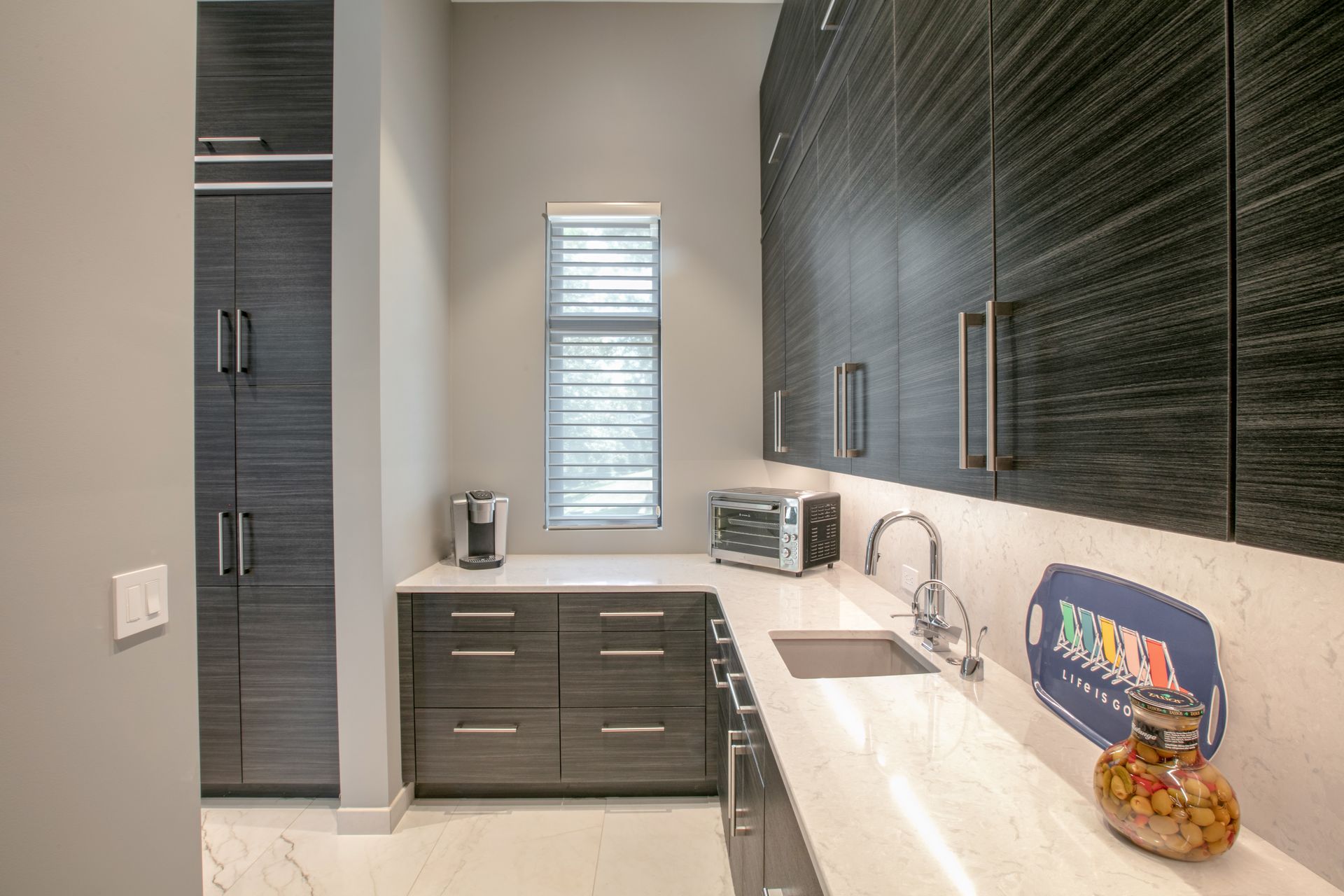 A modern kitchen area with dark cabinetry, white countertop, sink, and toaster oven.