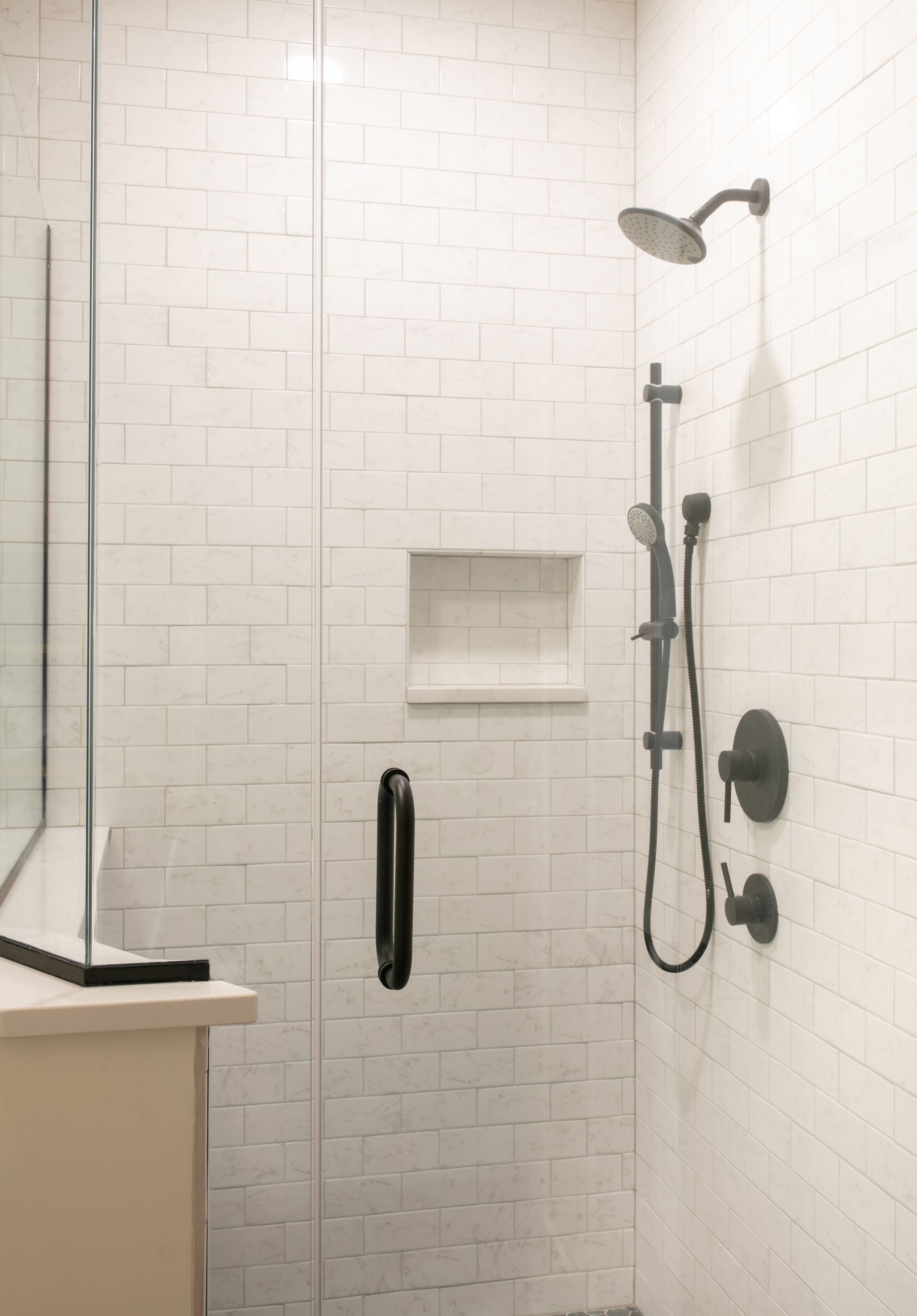 White tiled shower with black fixtures and glass door.