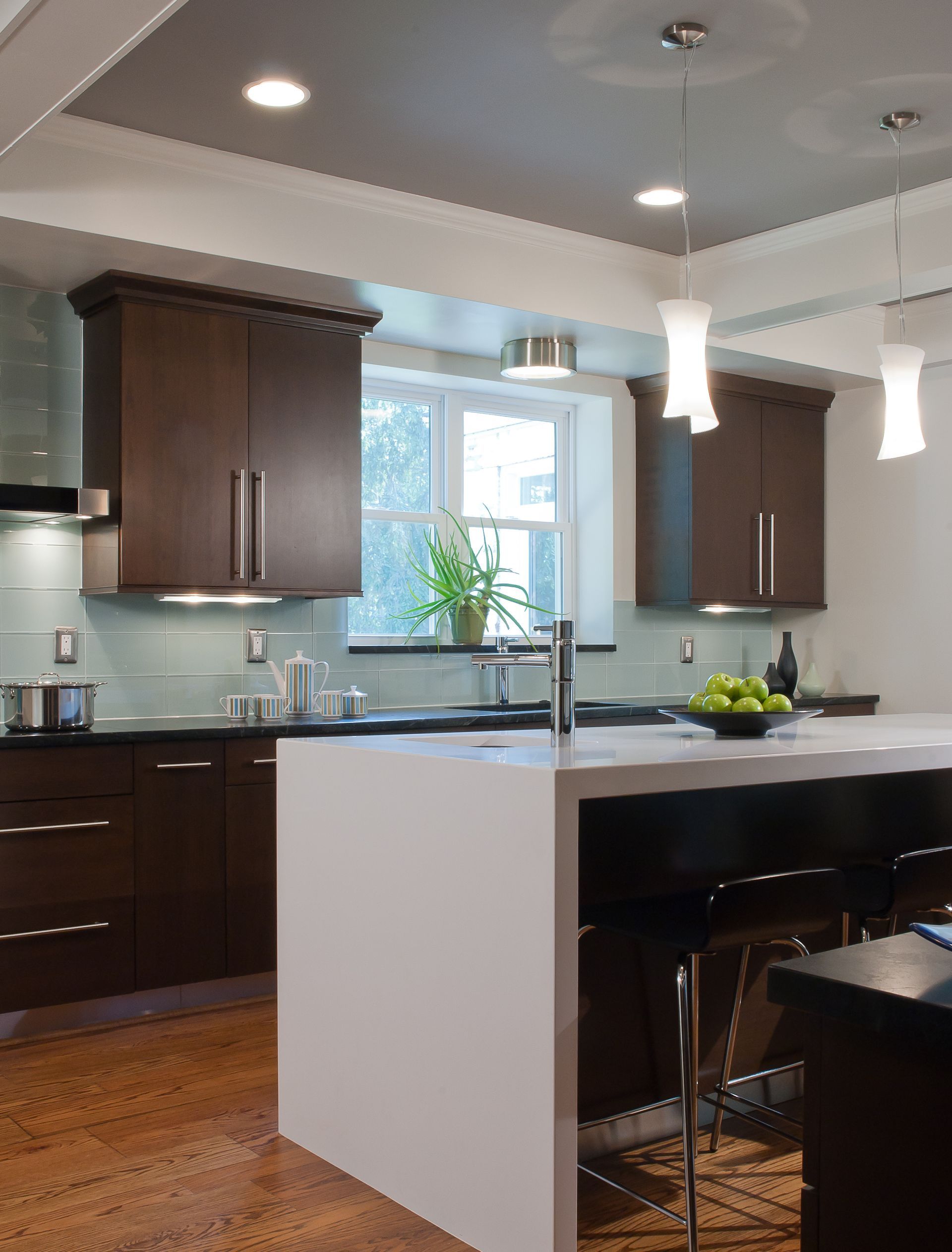 Modern kitchen with dark brown cabinets, white island, and light fixtures.