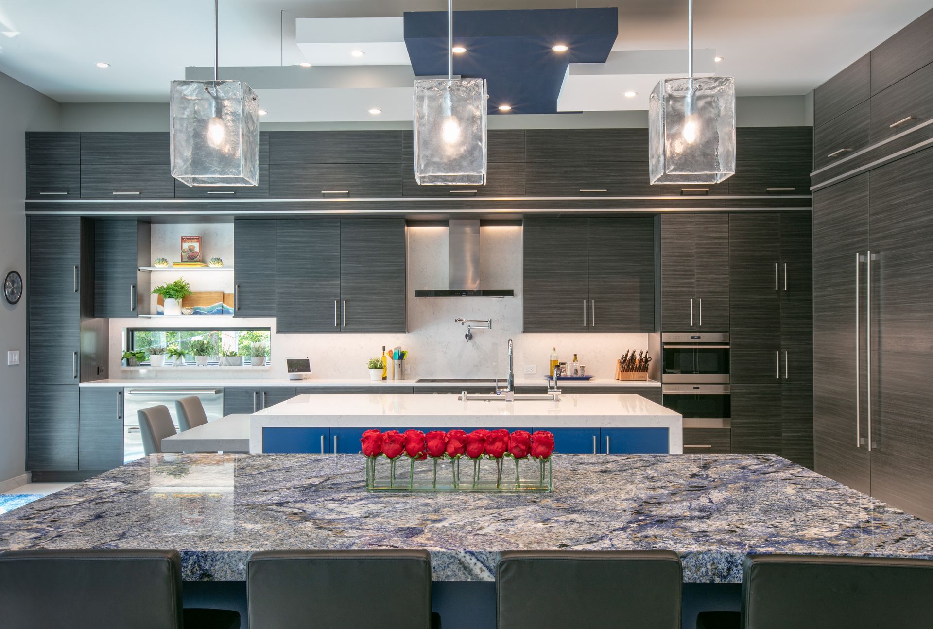 Modern kitchen with dark cabinetry, blue island, and glass pendant lights.