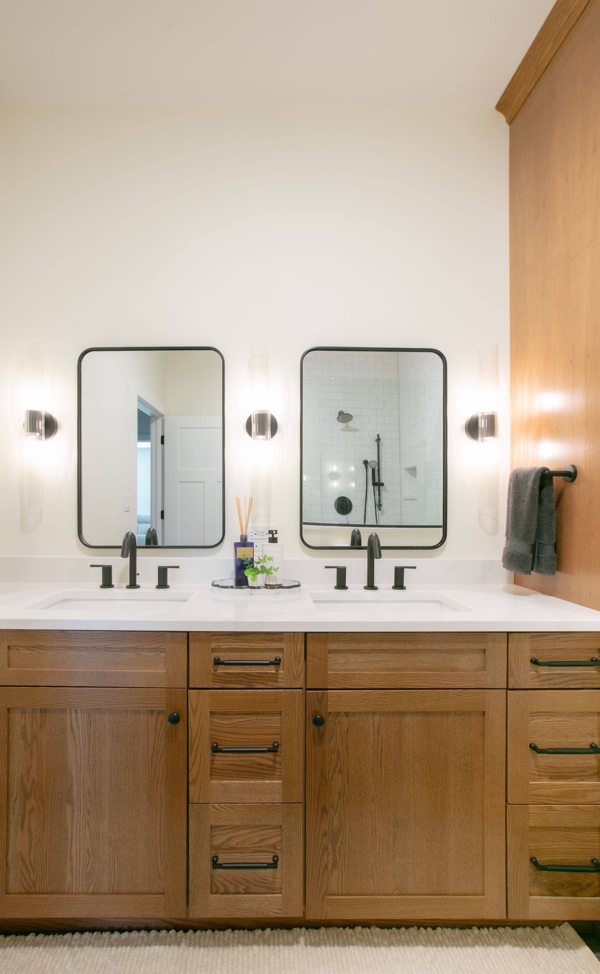 Double bathroom vanity with wood cabinets, black mirrors, sconces, and white countertop.