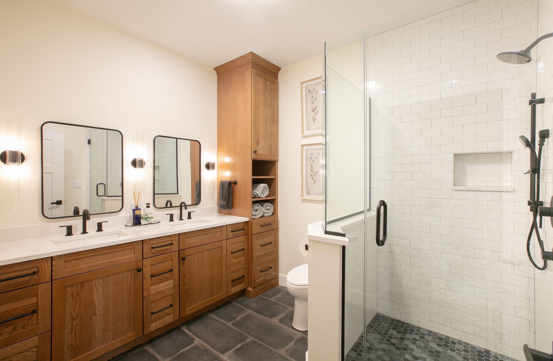 Bathroom with wood vanity, black fixtures, tiled shower, and a glass door.