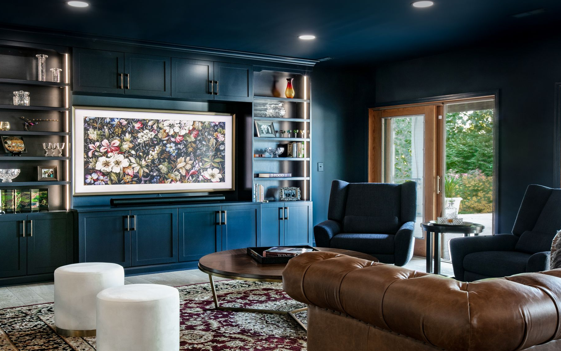Dark blue media room with built-in cabinetry, a floral TV, leather sofa, and two armchairs facing a doorway.