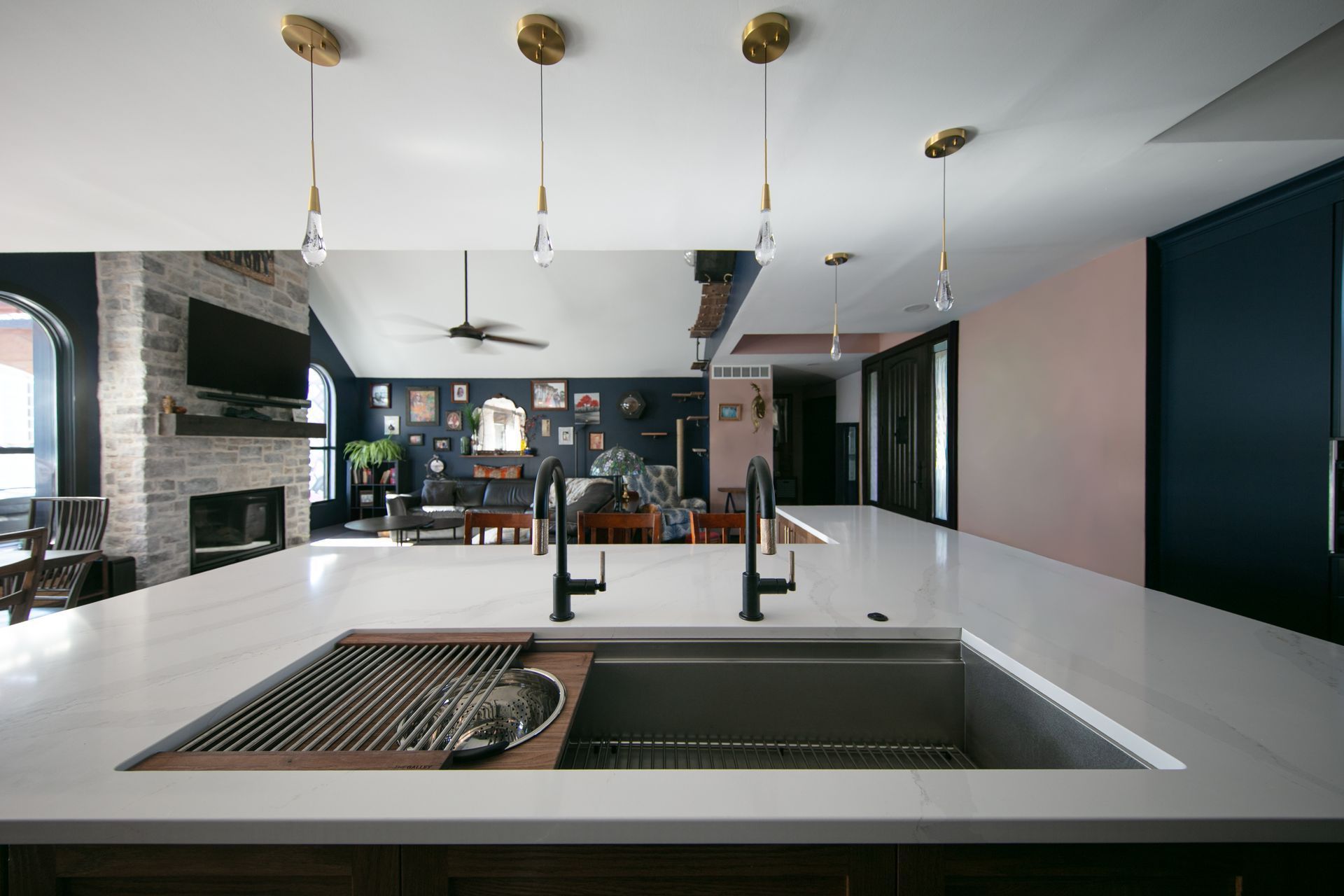 Modern kitchen with white countertop, black faucets, and pendant lights; living room with fireplace in the background.