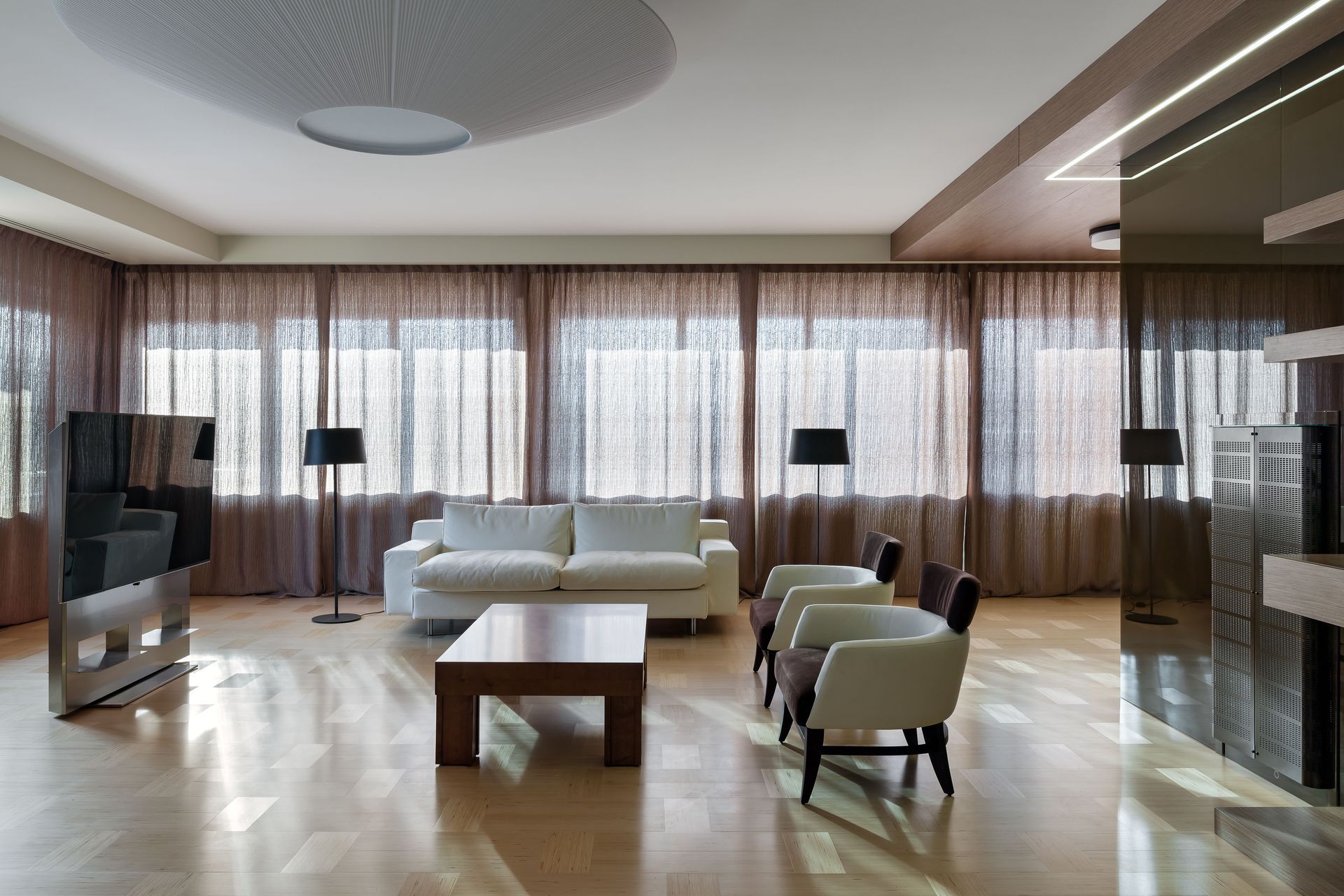 Modern living room with a white sofa, chairs, and brown curtains.