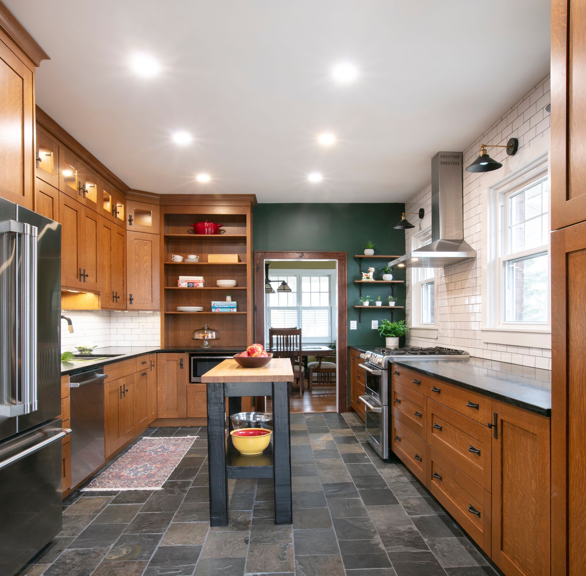 Kitchen with dark cabinetry, slate floors, and a small island. Dark green wall and open doorway.