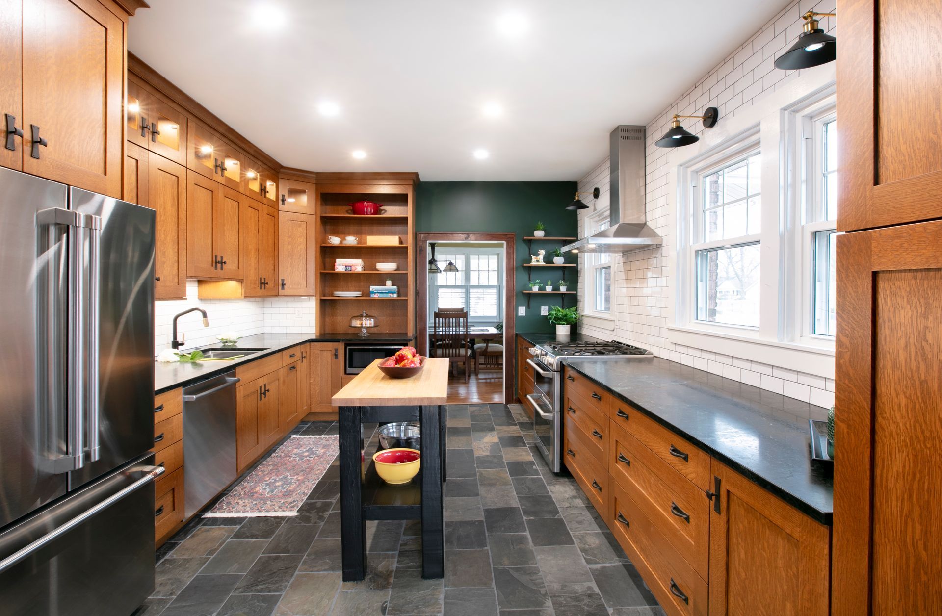 Wooden kitchen with stainless steel appliances, dark countertops, and slate flooring.