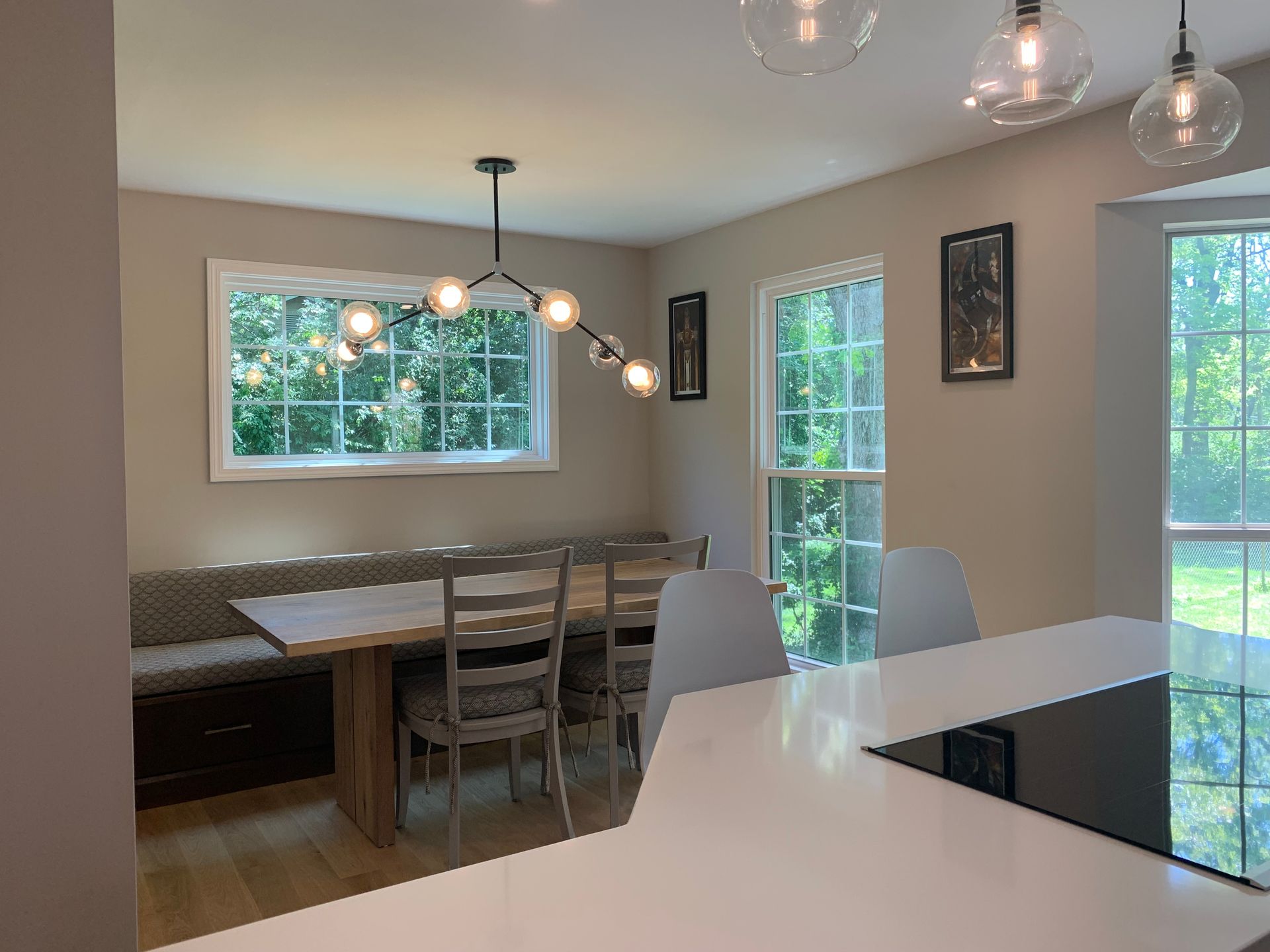 Dining area with built-in bench, wooden table and chairs, pendant lights, windows, and neutral walls.