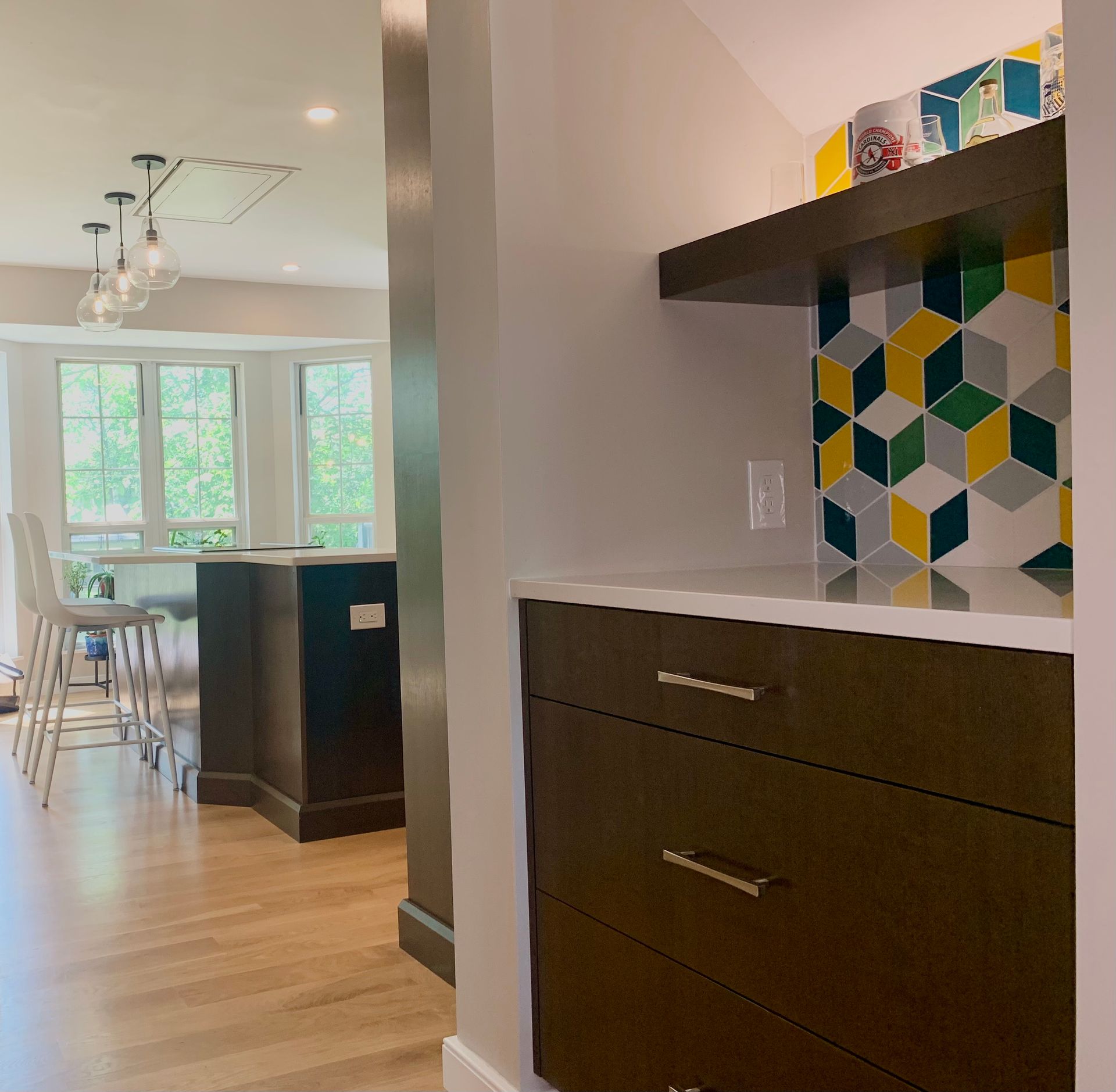 Interior view of a kitchen. Dark cabinets, white countertop, and colorful tile backsplash.