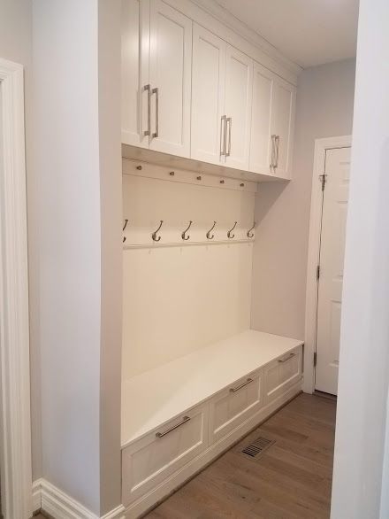 White built-in storage unit with cabinets, hooks, bench, and drawers in a hallway.