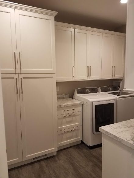 Laundry room with white cabinets, washer and dryer. Light granite countertops, wood-look floor.