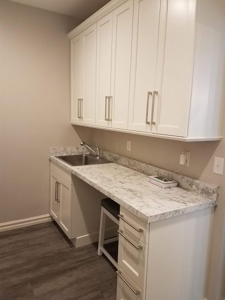 White cabinetry with a granite countertop, sink, and drawers in a room with a stool.