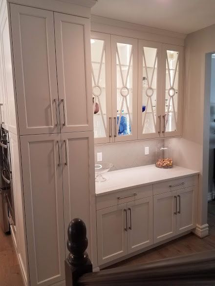 White built-in cabinetry with a countertop, glass-front display cabinets, and tall storage on a staircase landing.
