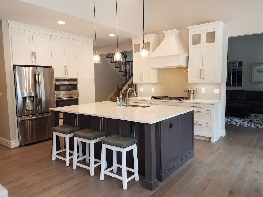 Modern kitchen with white cabinets, dark island, stainless steel appliances, and wooden floor.