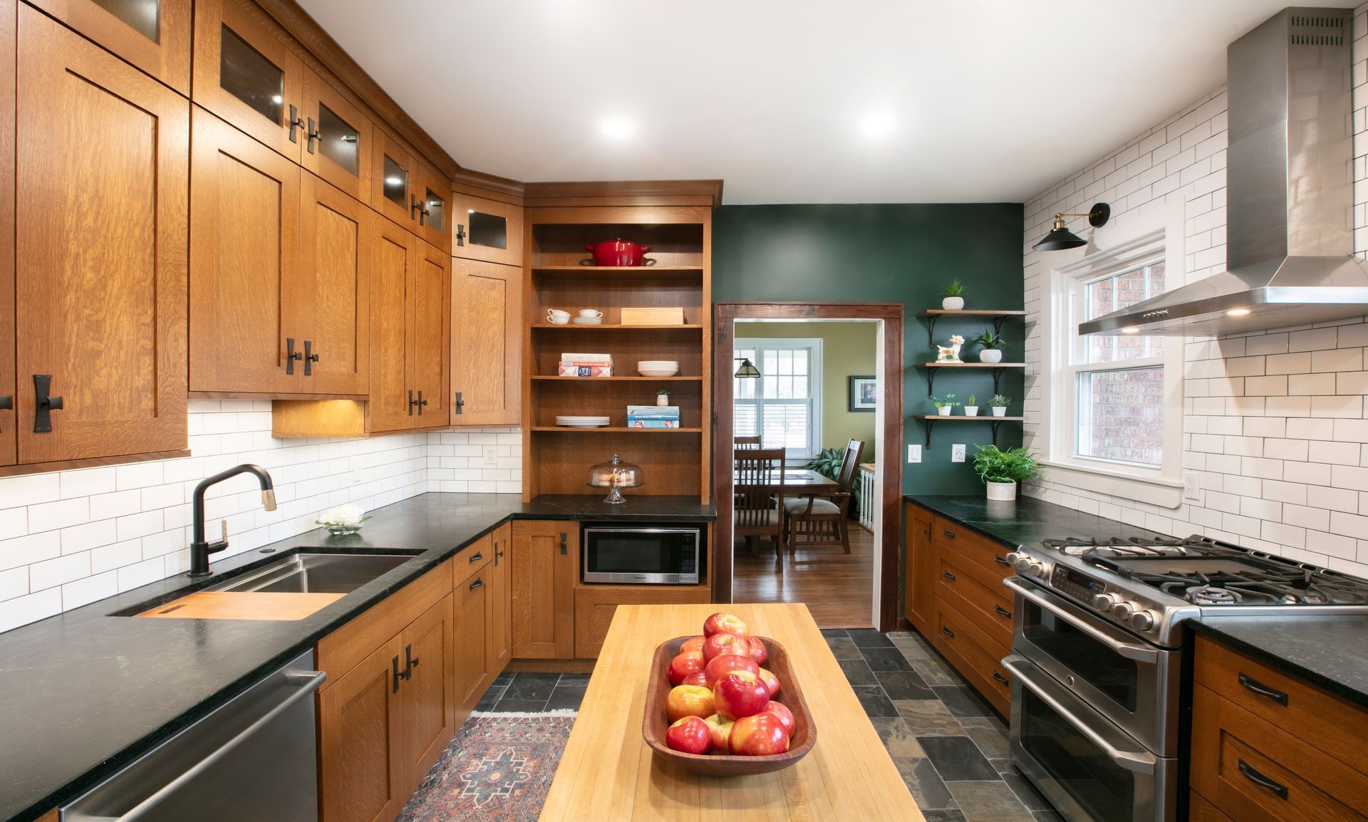 Kitchen with wood cabinets, black countertops, and a central island with a bowl of apples.