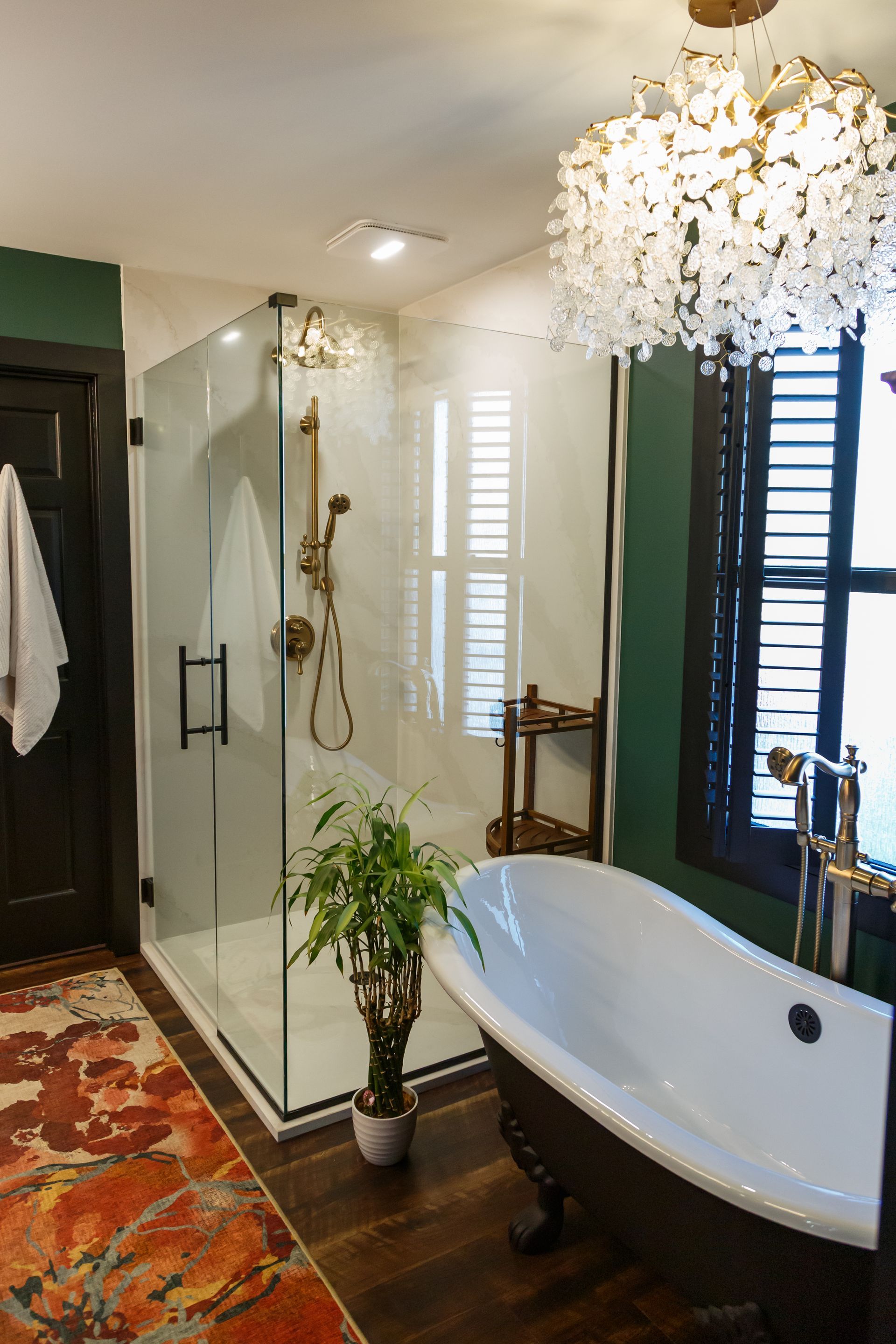Bathroom with a glass shower, clawfoot tub, dark green walls, and ornate chandelier.