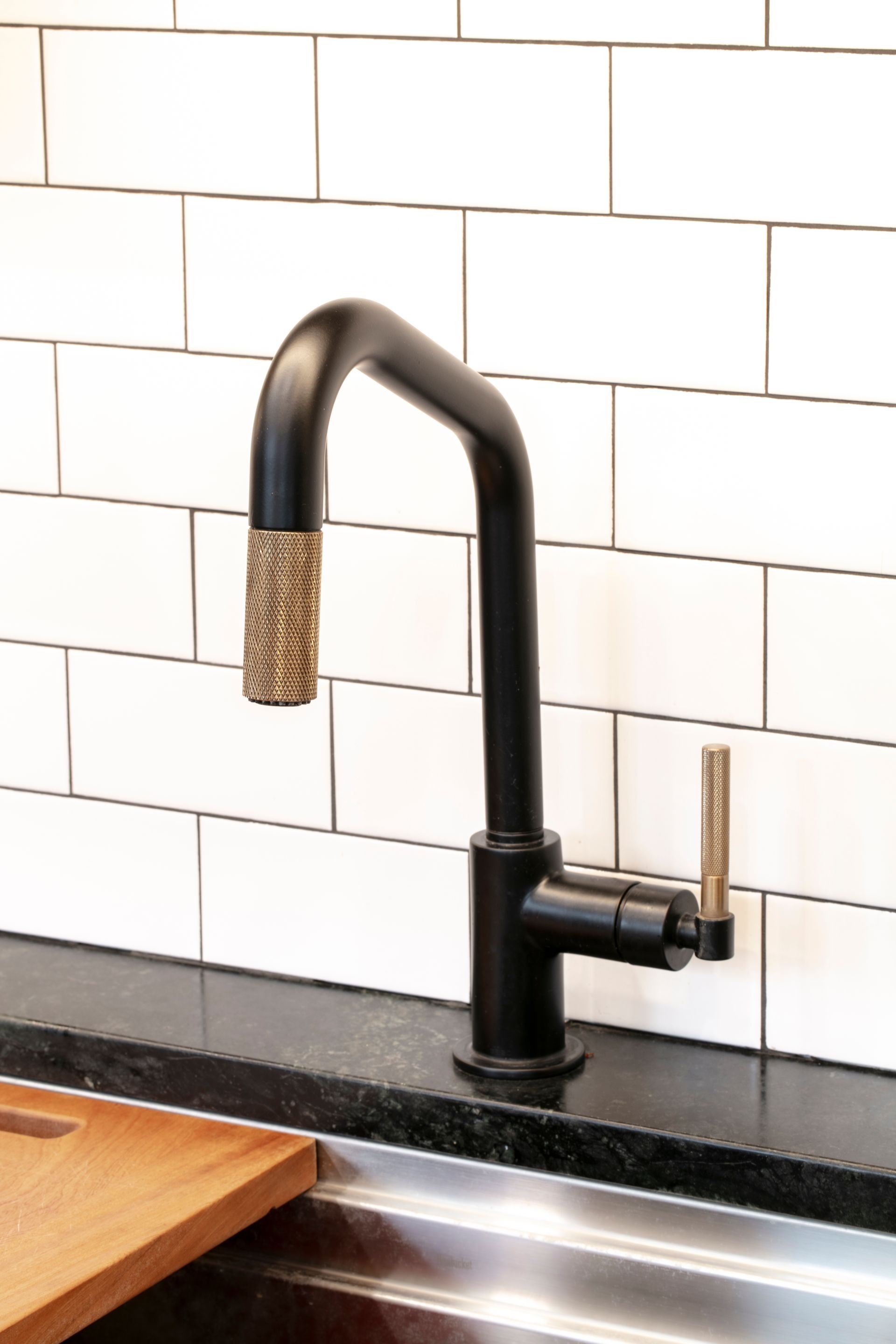 Black kitchen faucet with a textured, golden nozzle and lever, set against white subway tiles.