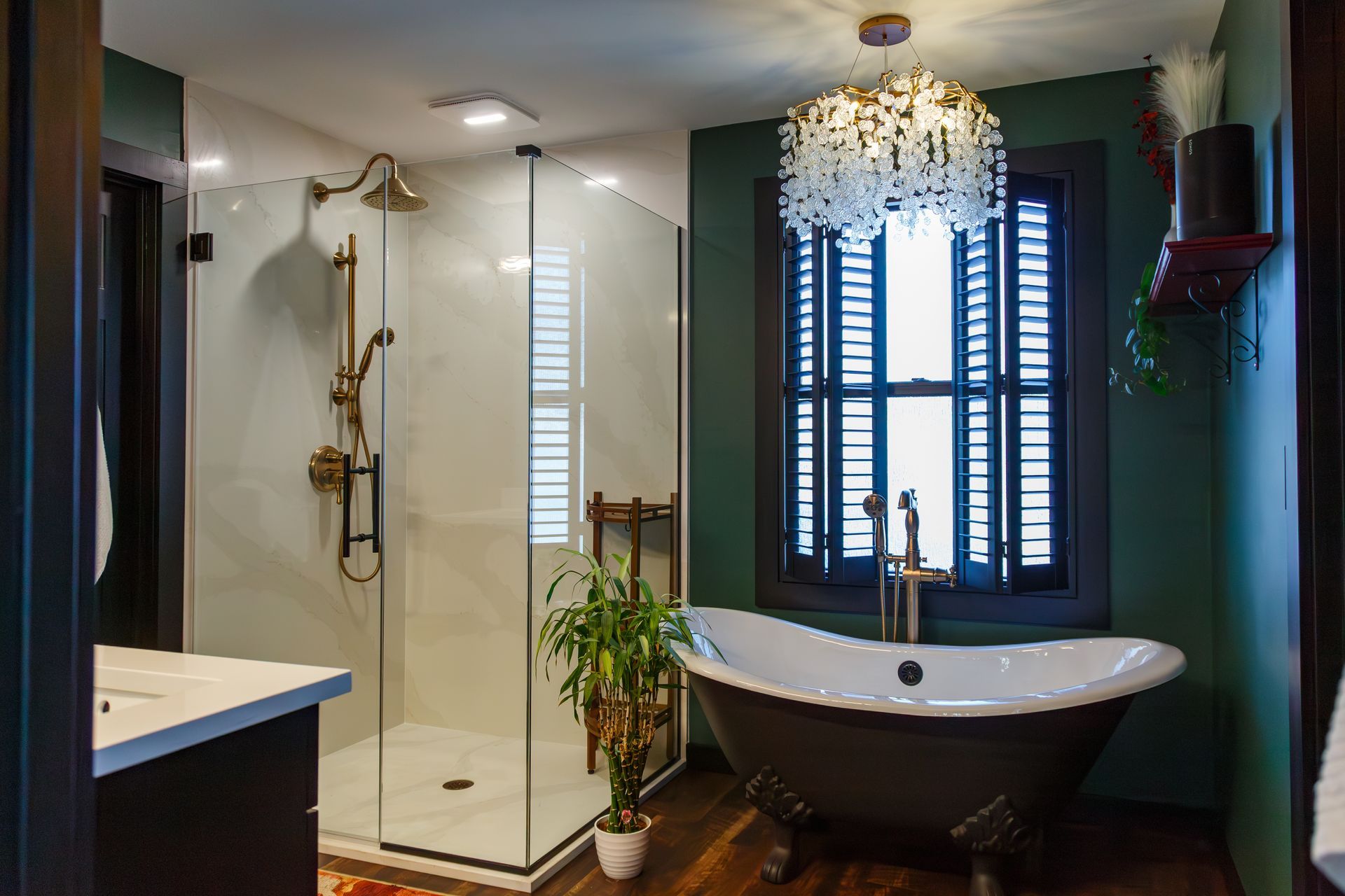 Bathroom with clawfoot tub, glass shower, green walls, and decorative chandelier.