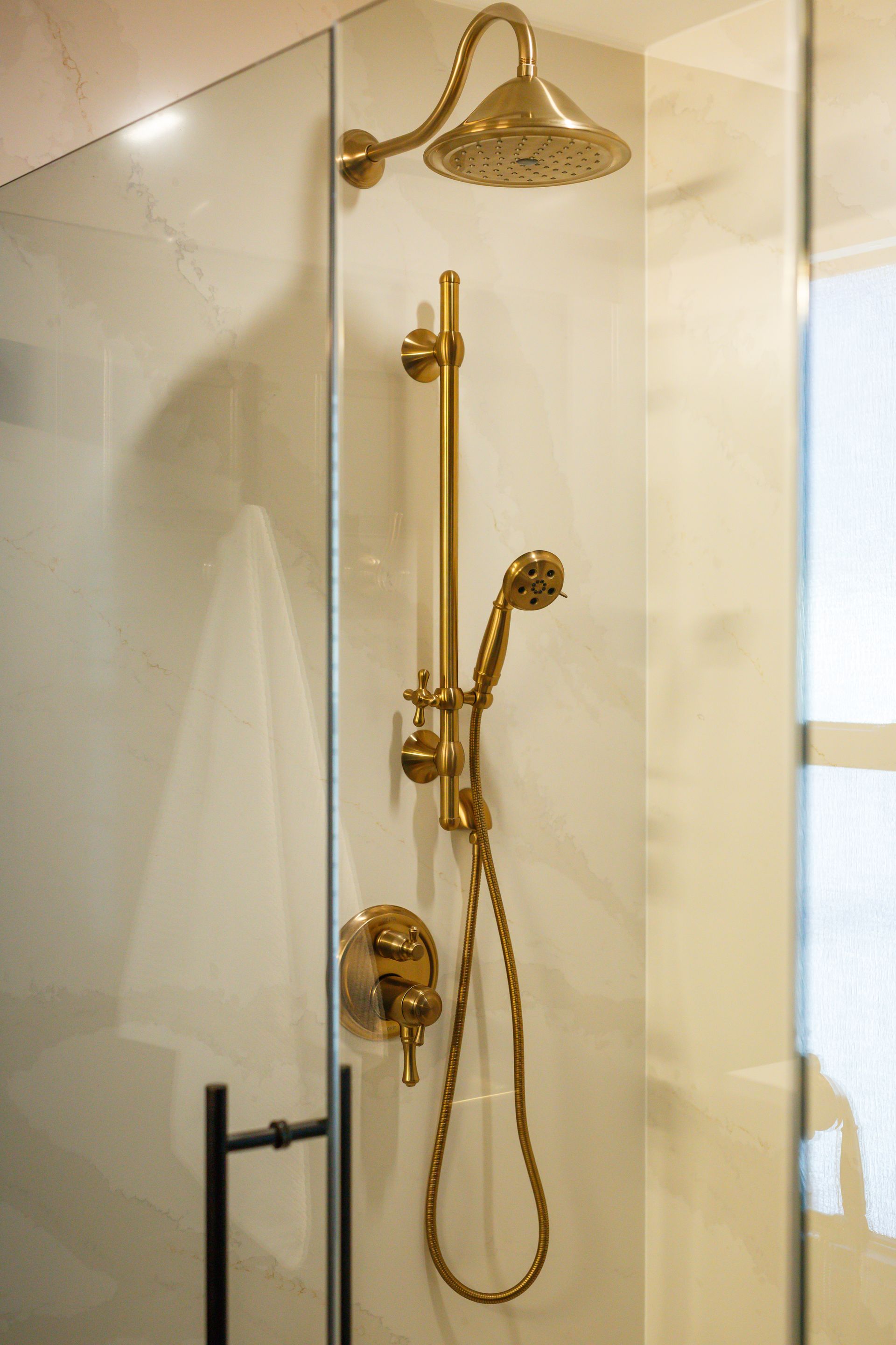Gold showerhead and handheld shower fixtures against marble tile in a shower.