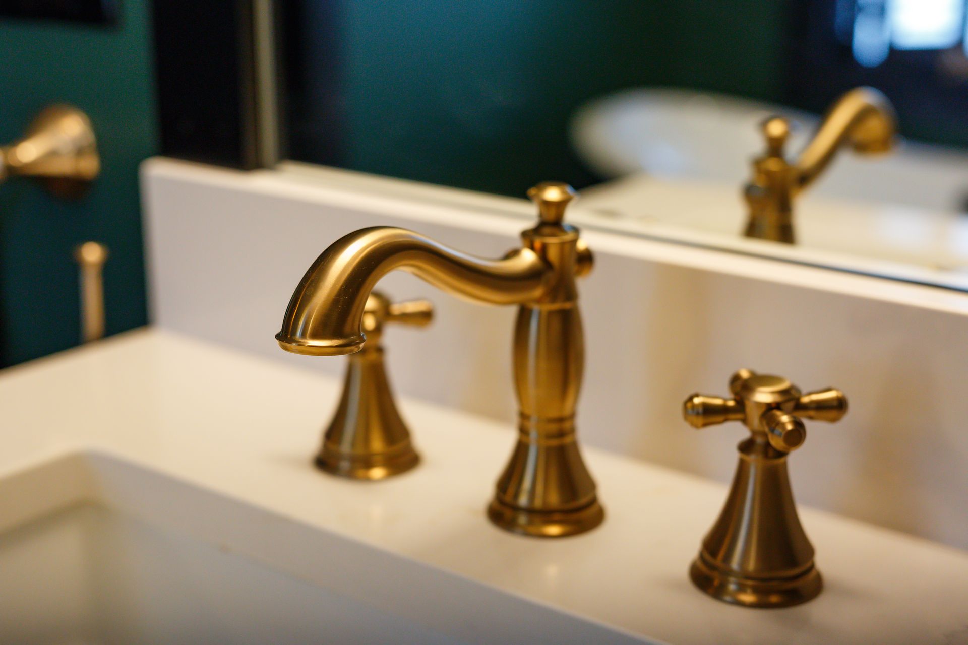 Gold bathroom faucet with two handles on a white countertop; a mirror reflects the faucet.