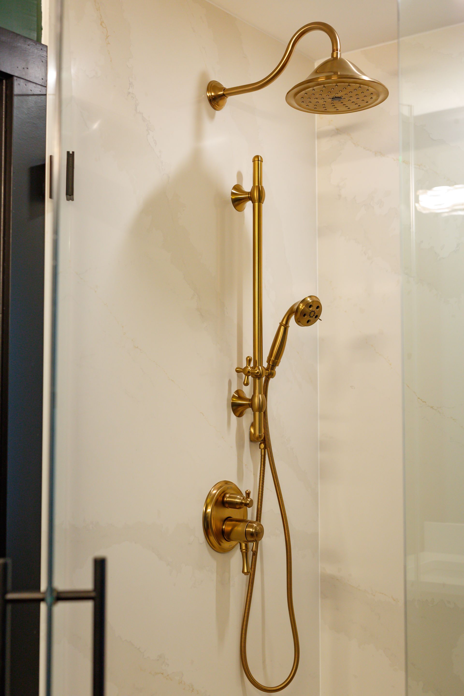 Gold shower fixtures on a white tiled wall. A handheld shower head is attached.