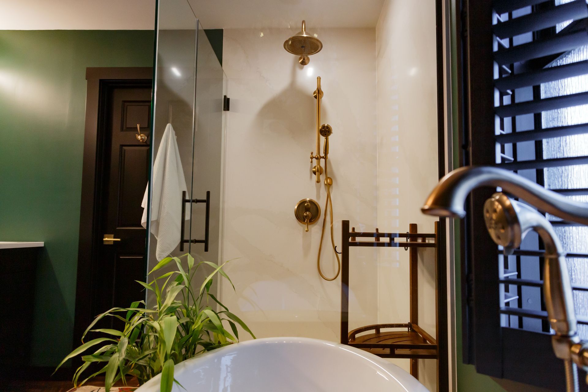 Bathroom with gold shower fixtures, dark door, green wall, and white tub.