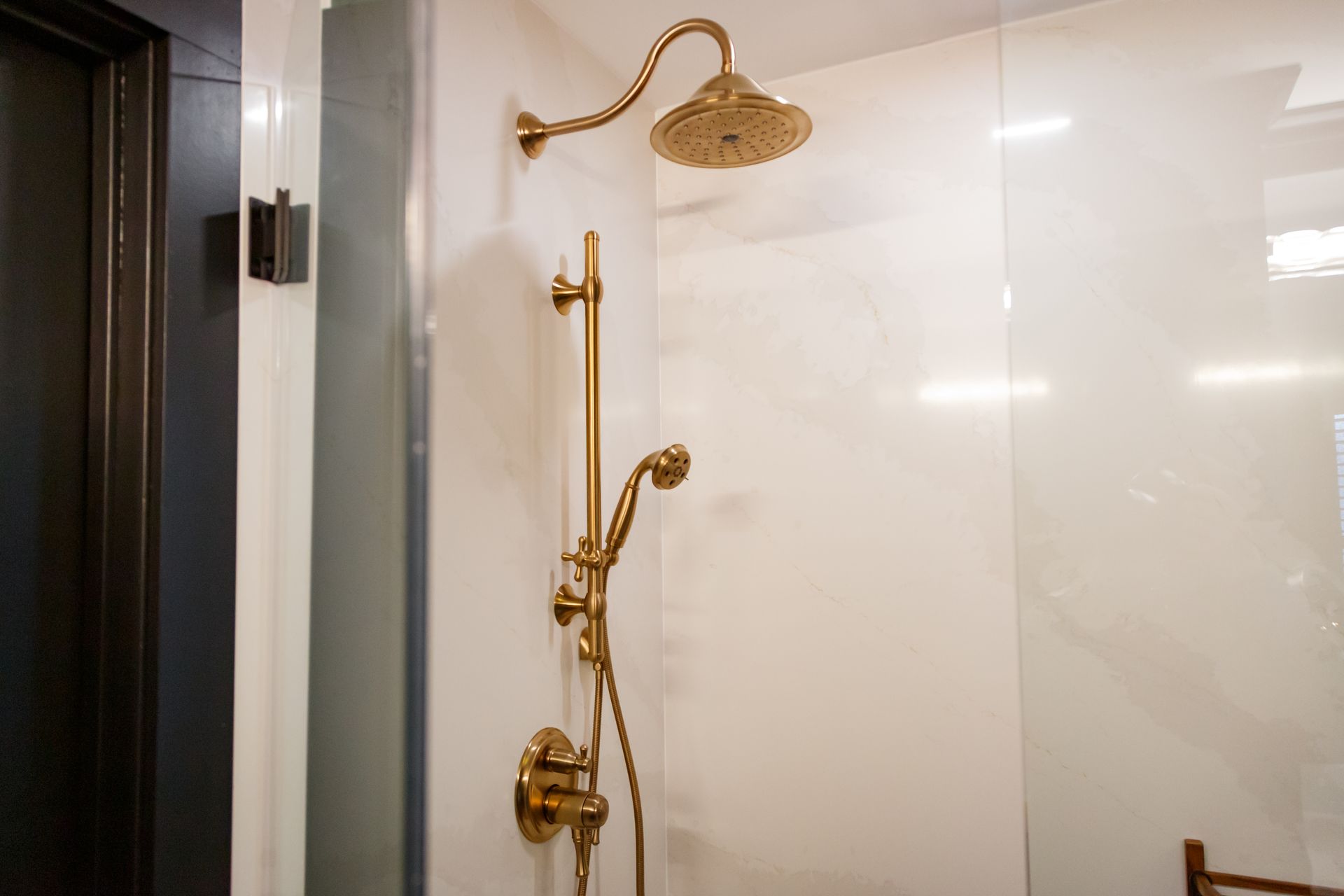 Gold shower fixtures on a white tiled wall. A handheld shower and overhead rain shower.