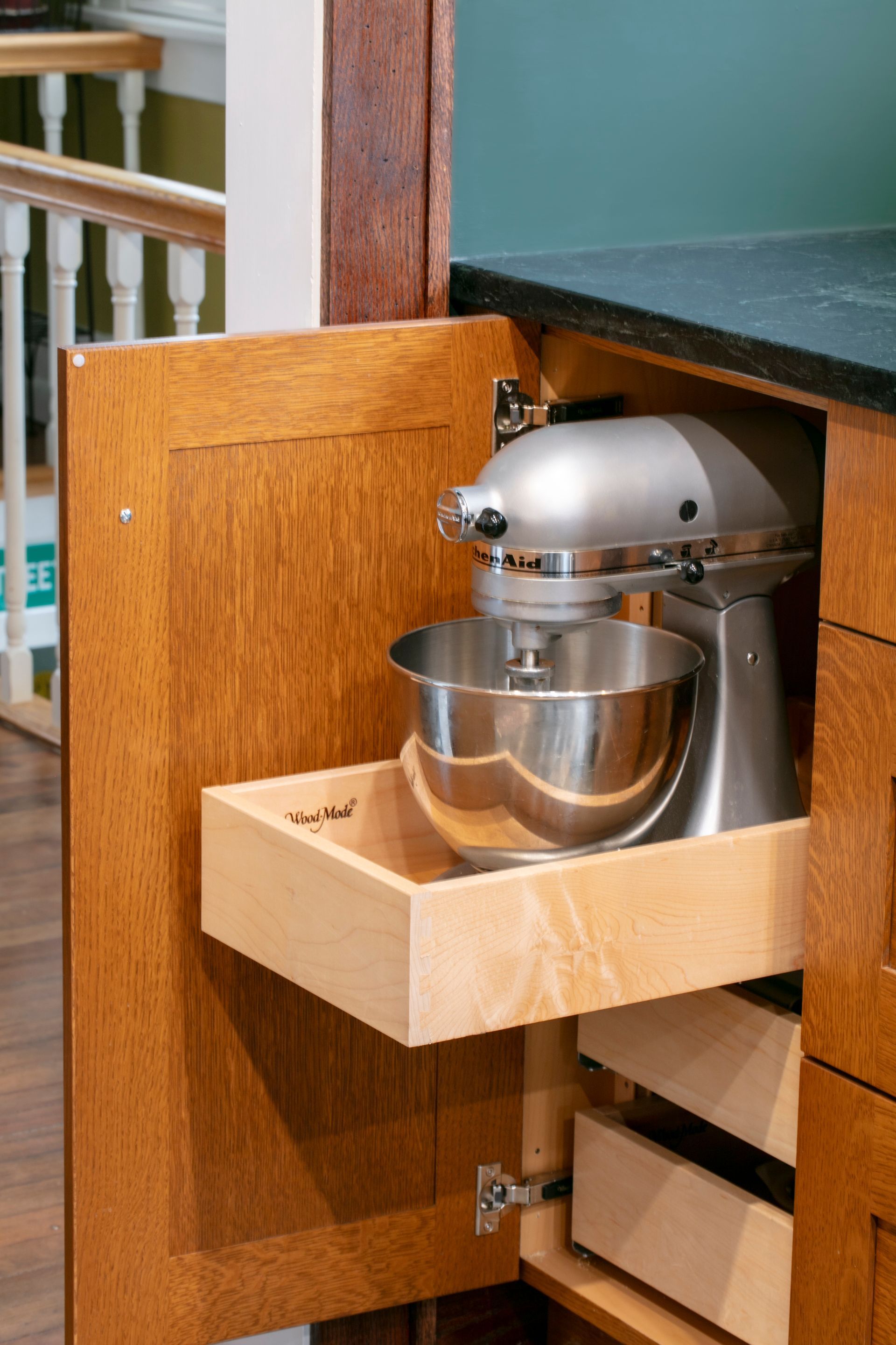 Kitchen cabinet with pull-out tray holding a silver KitchenAid mixer. Cabinet door open, brown wood.