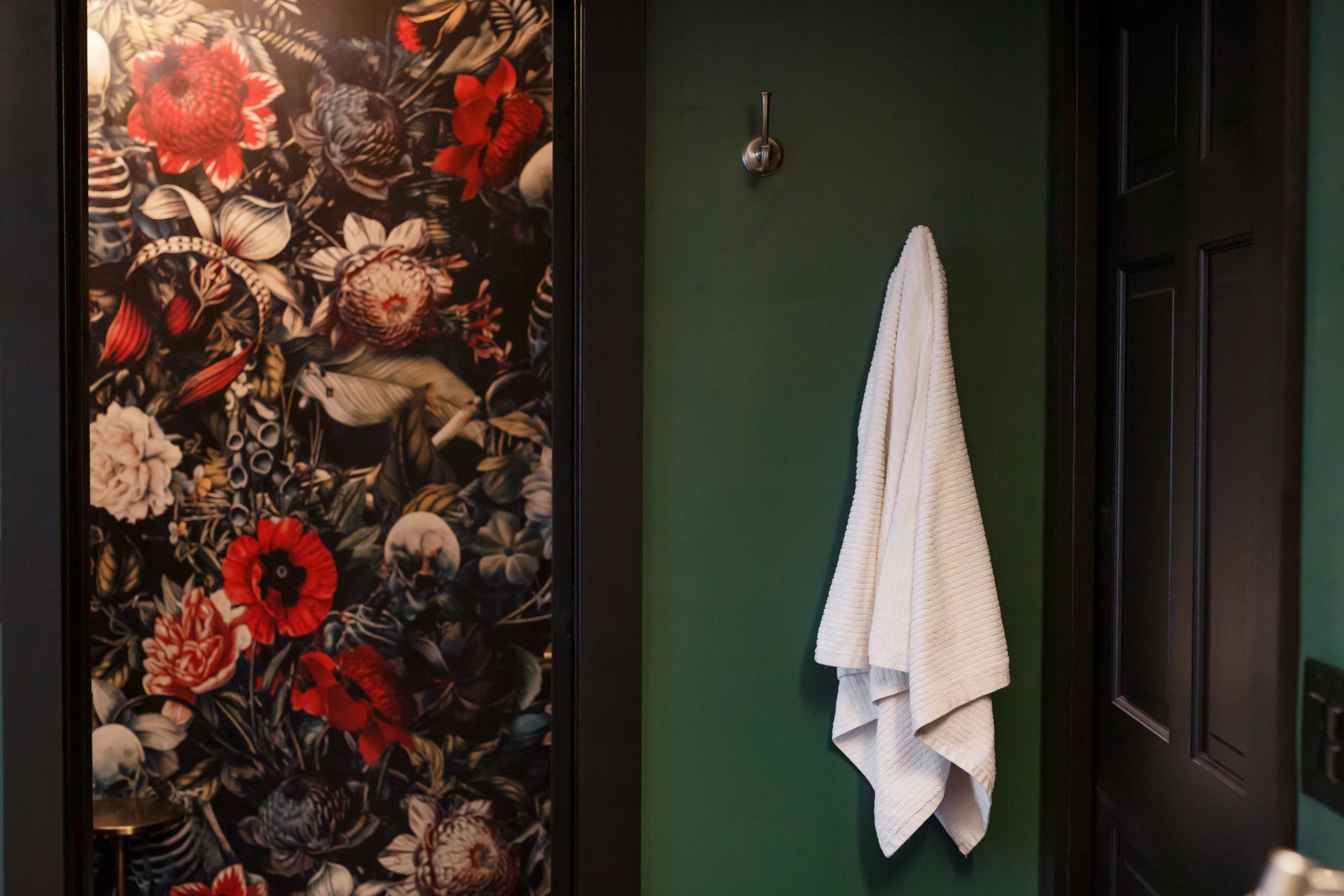 Bathroom interior with floral wallpapered door, dark green wall, towel on hook, black door.