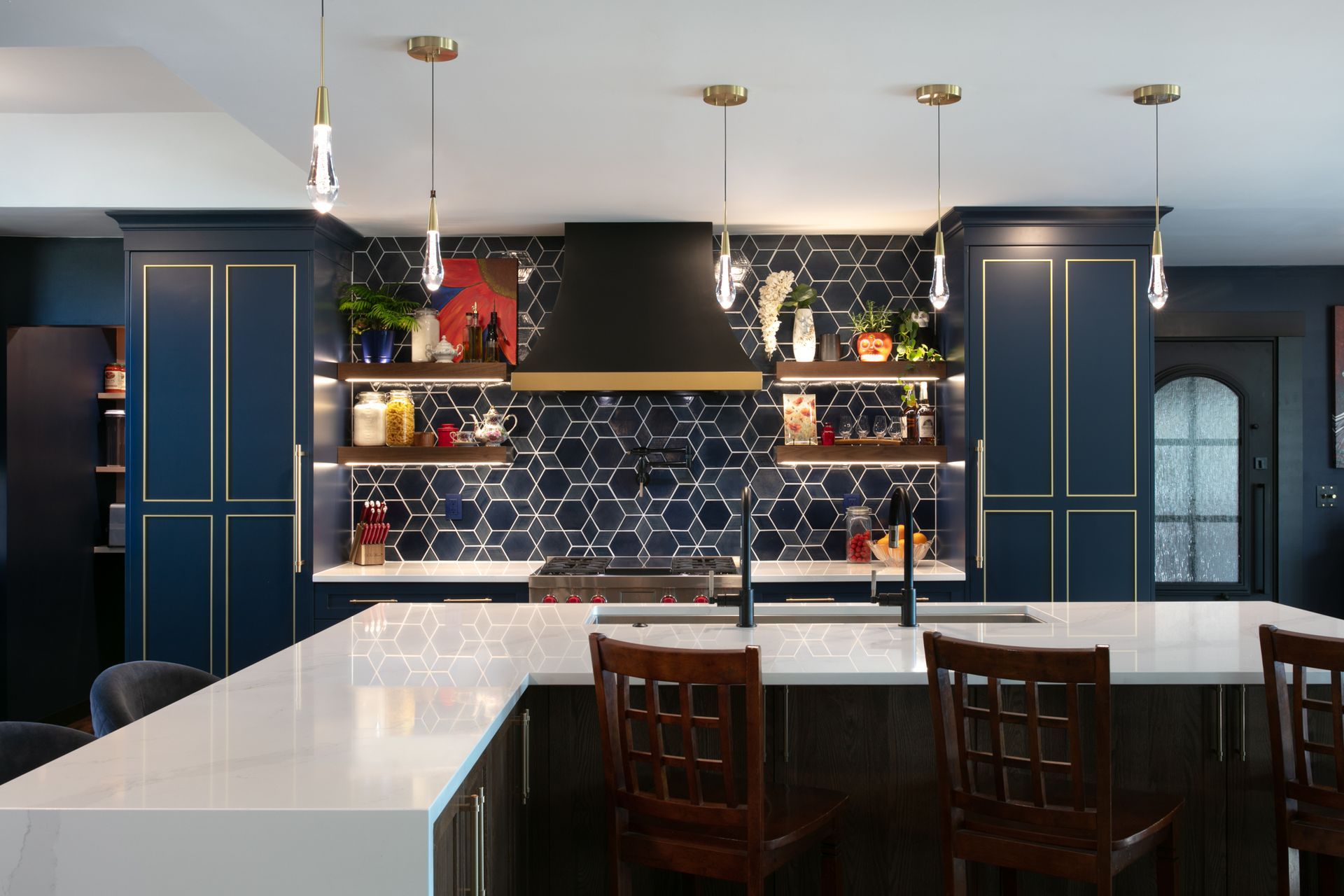 Blue kitchen with white countertops, dark cabinetry, hexagon backsplash, and hanging pendant lights.