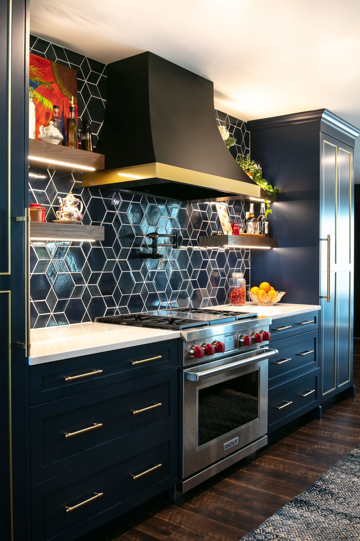 Navy blue kitchen with gold accents and a stainless steel oven. Dark hexagon tile backsplash.